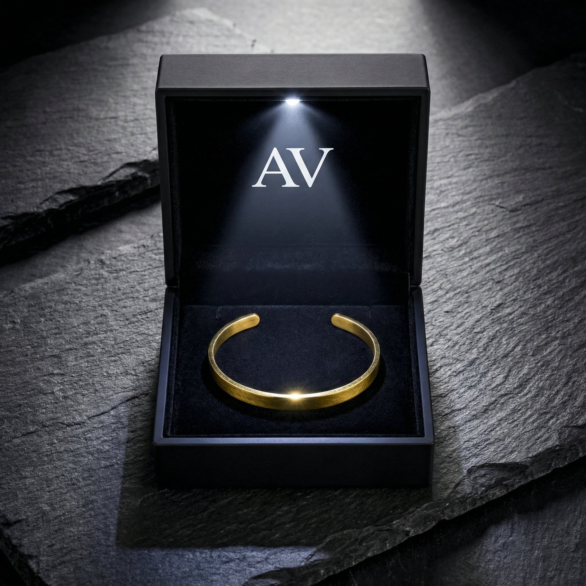 Gold stainless steel cuff bracelet presented in a black LED-lit jewelry box on a stone surface.