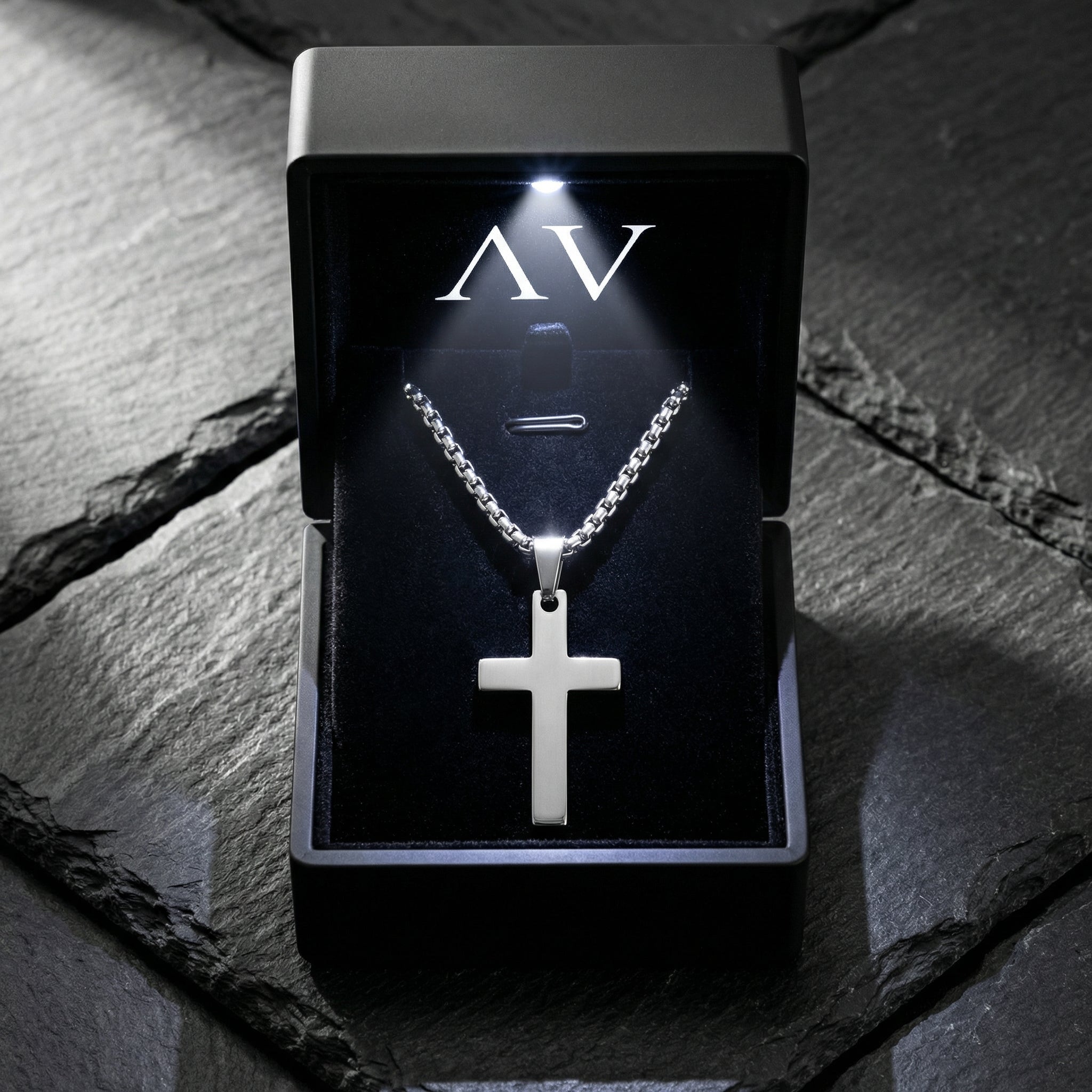 Silver stainless steel Apostle Cross necklace inside a premium black illuminated gift box on a stone surface.