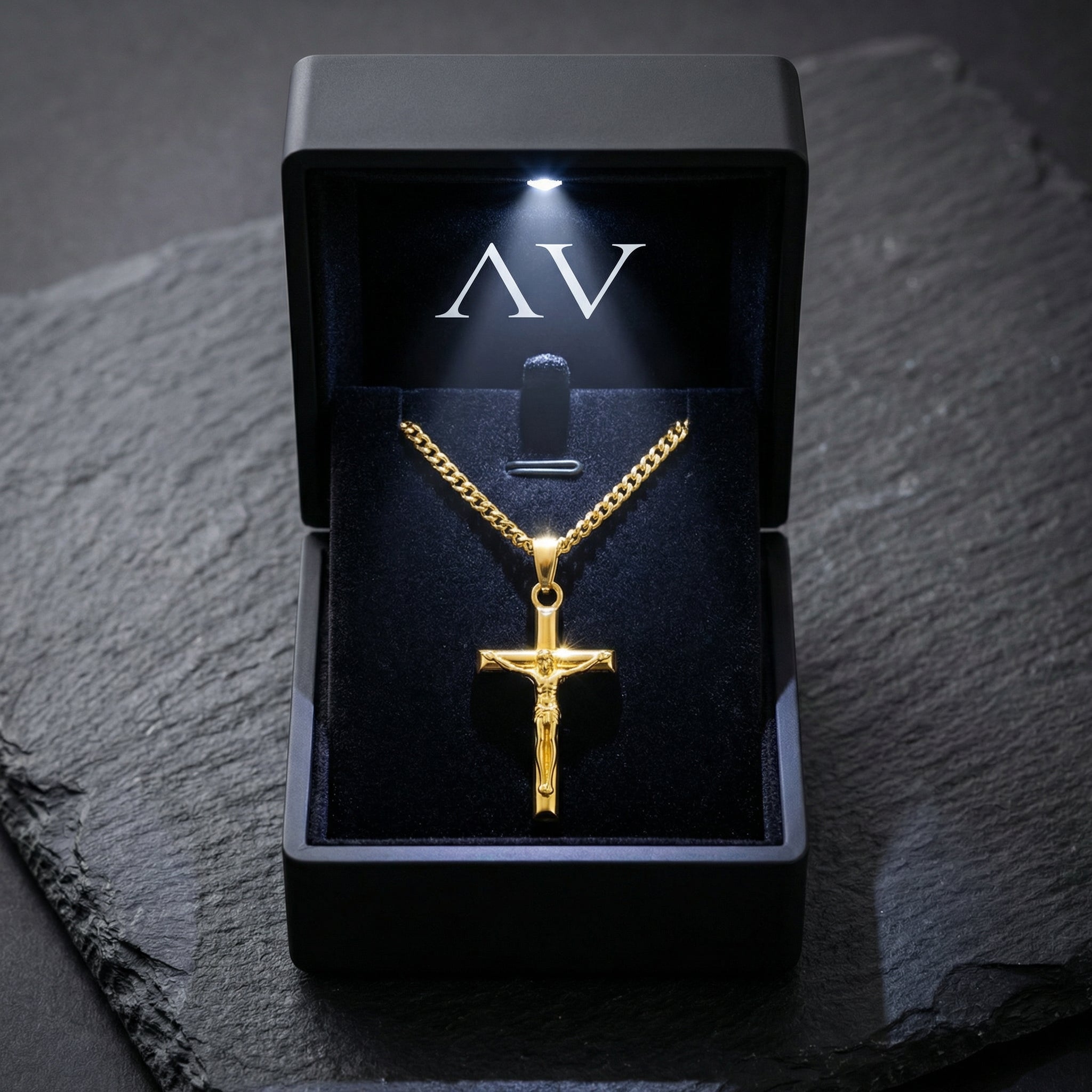 Gold stainless steel Divine Cross crucifix pendant in a black LED-lit jewelry box on a stone surface.