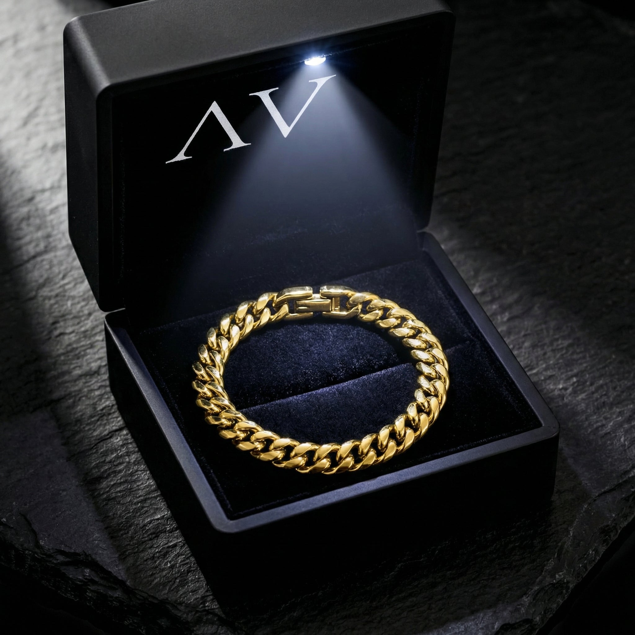 Gold stainless steel Cuban link bracelet inside a black LED-lit jewelry box on a stone surface.