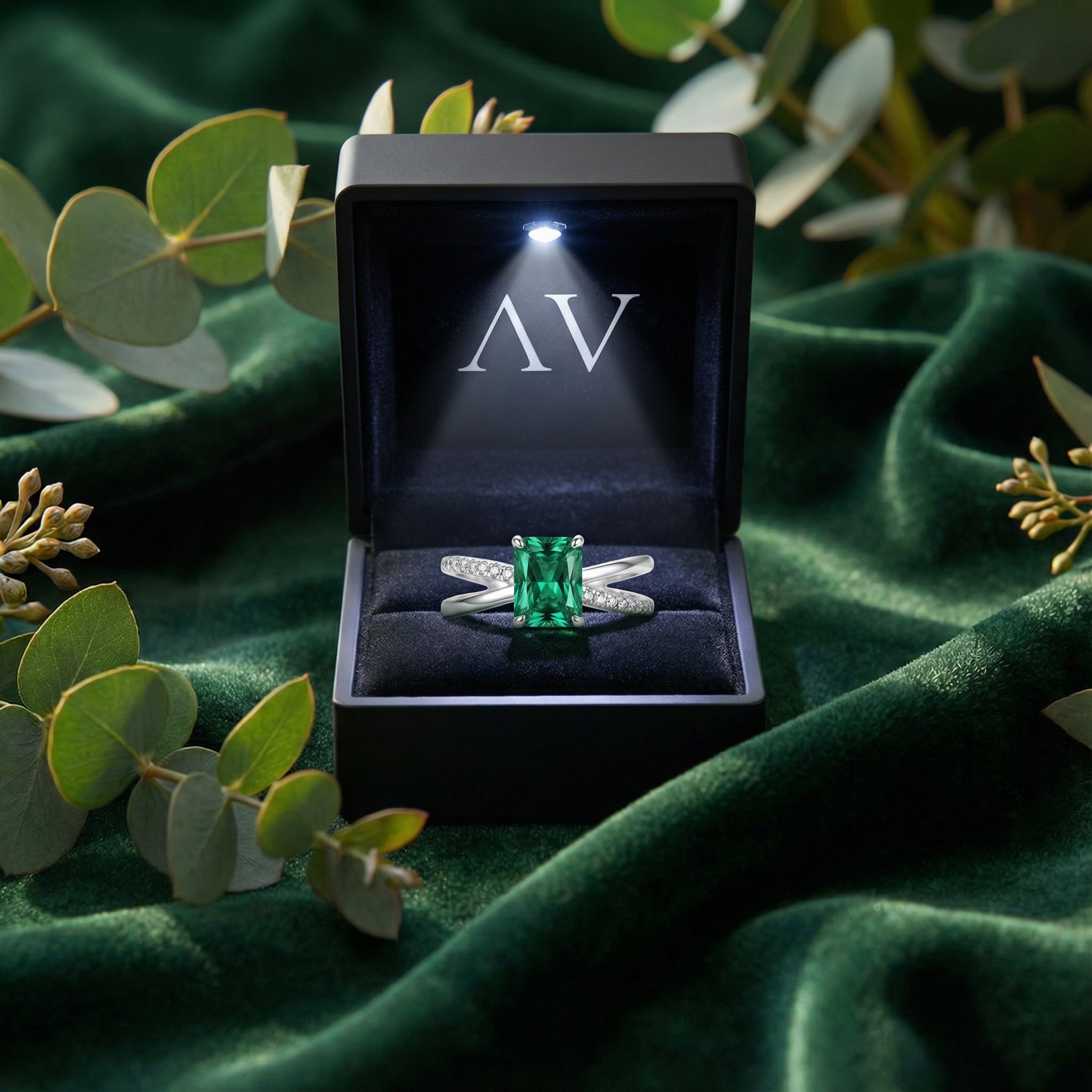 The Sylvana Twist Ring in S925 sterling silver with emerald cut green simulated emerald in a black LED-lit jewelry box.