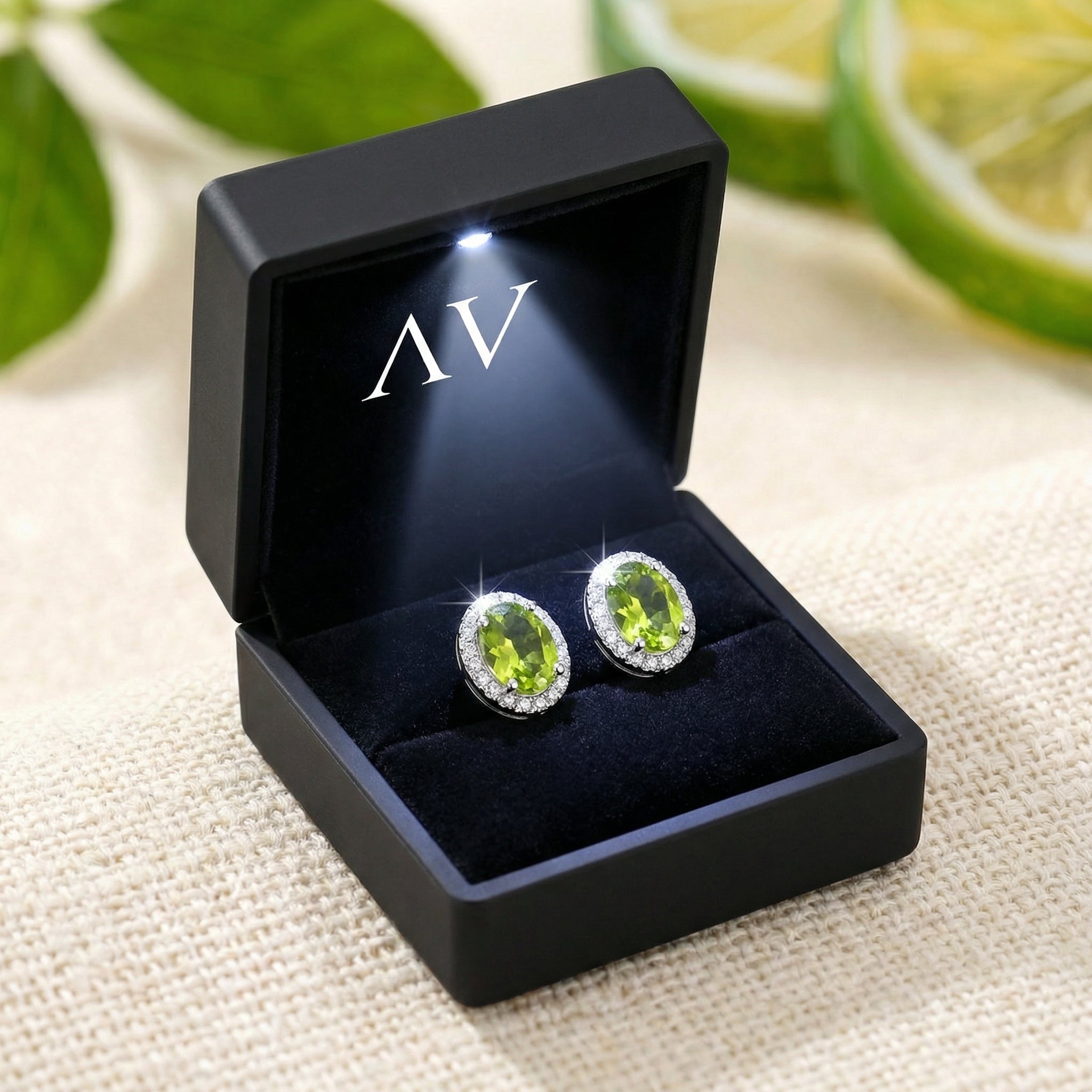 Oval peridot halo stud earrings presented in a luxury black LED-lit jewelry gift box.