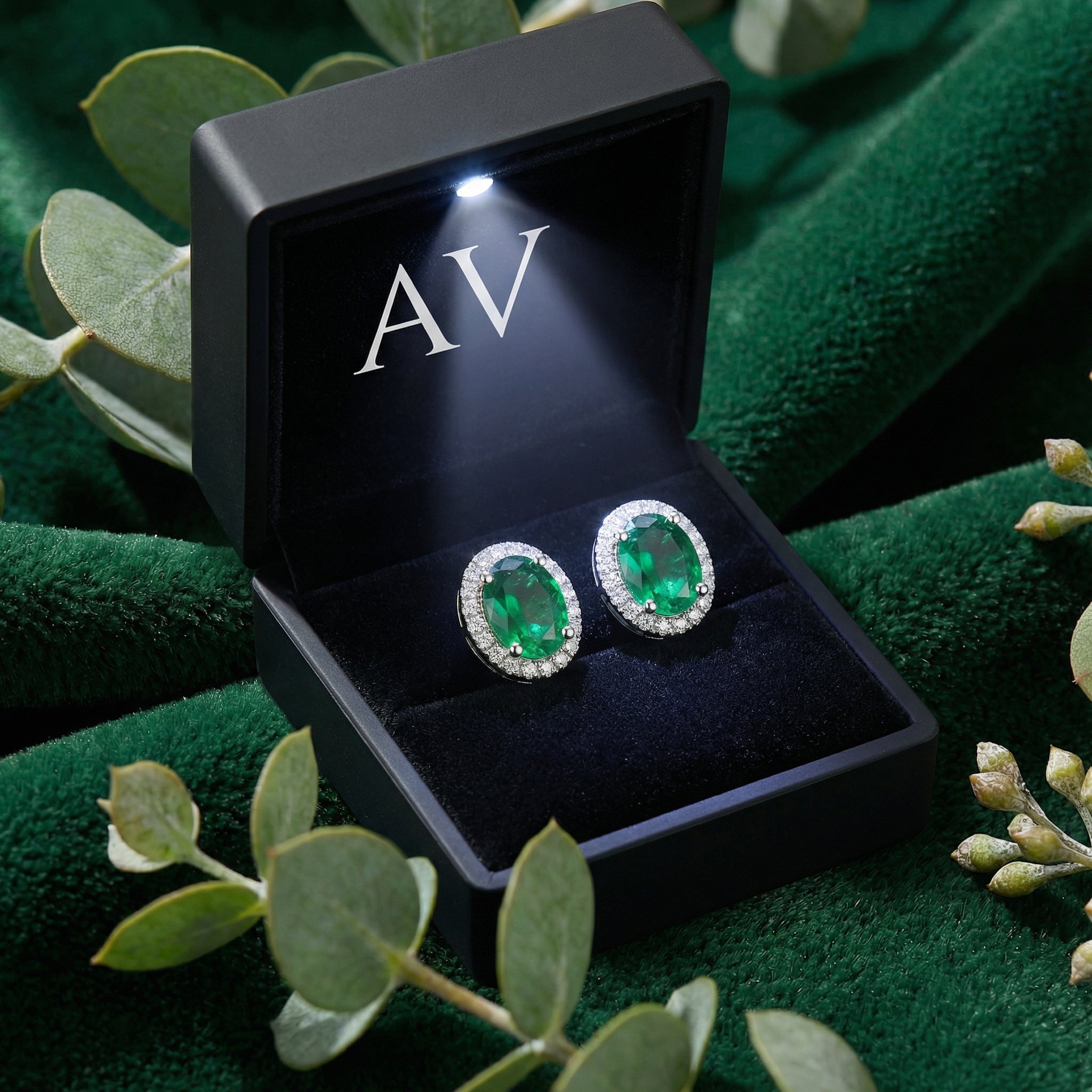 Pair of oval simulated emerald halo stud earrings in S925 sterling silver inside a black LED-lit gift box.