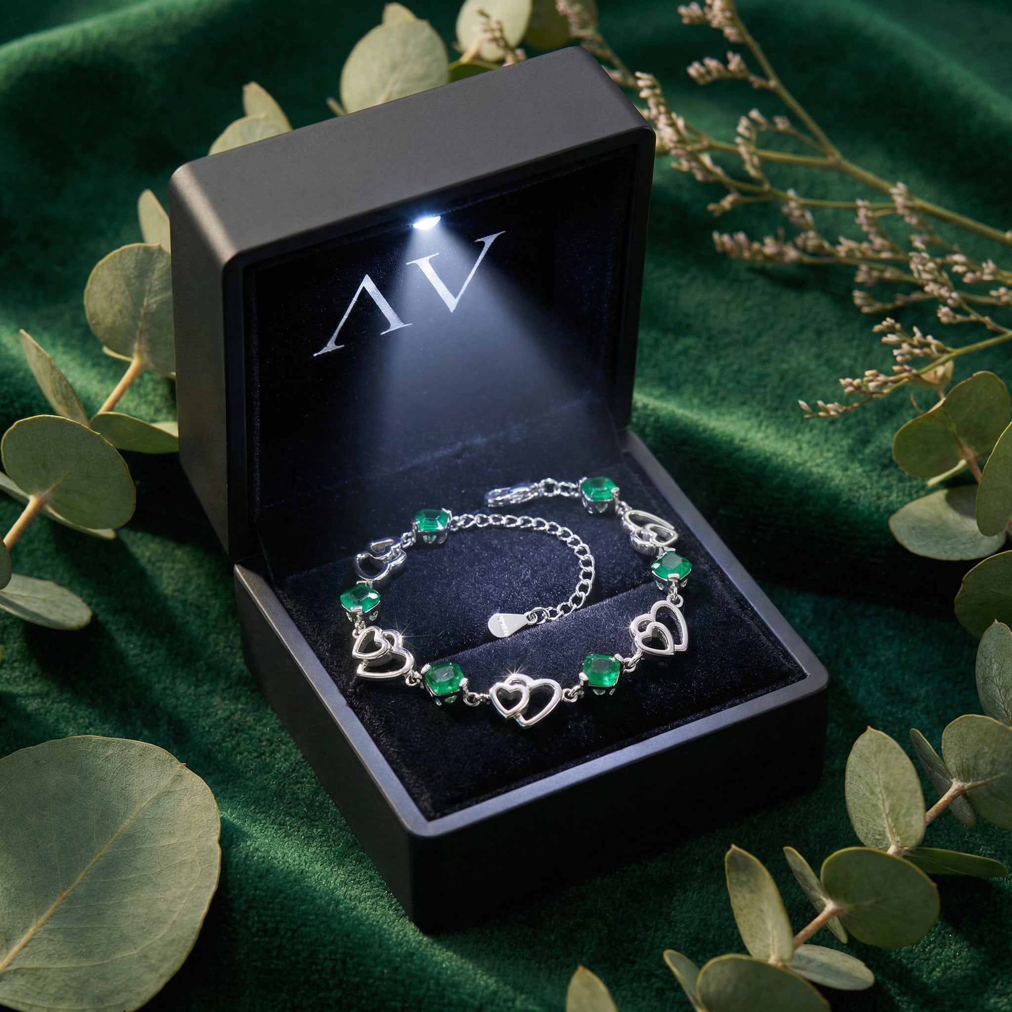 Sterling silver heart bracelet with cushion cut simulated emeralds presented in a black LED-lighted jewelry box.