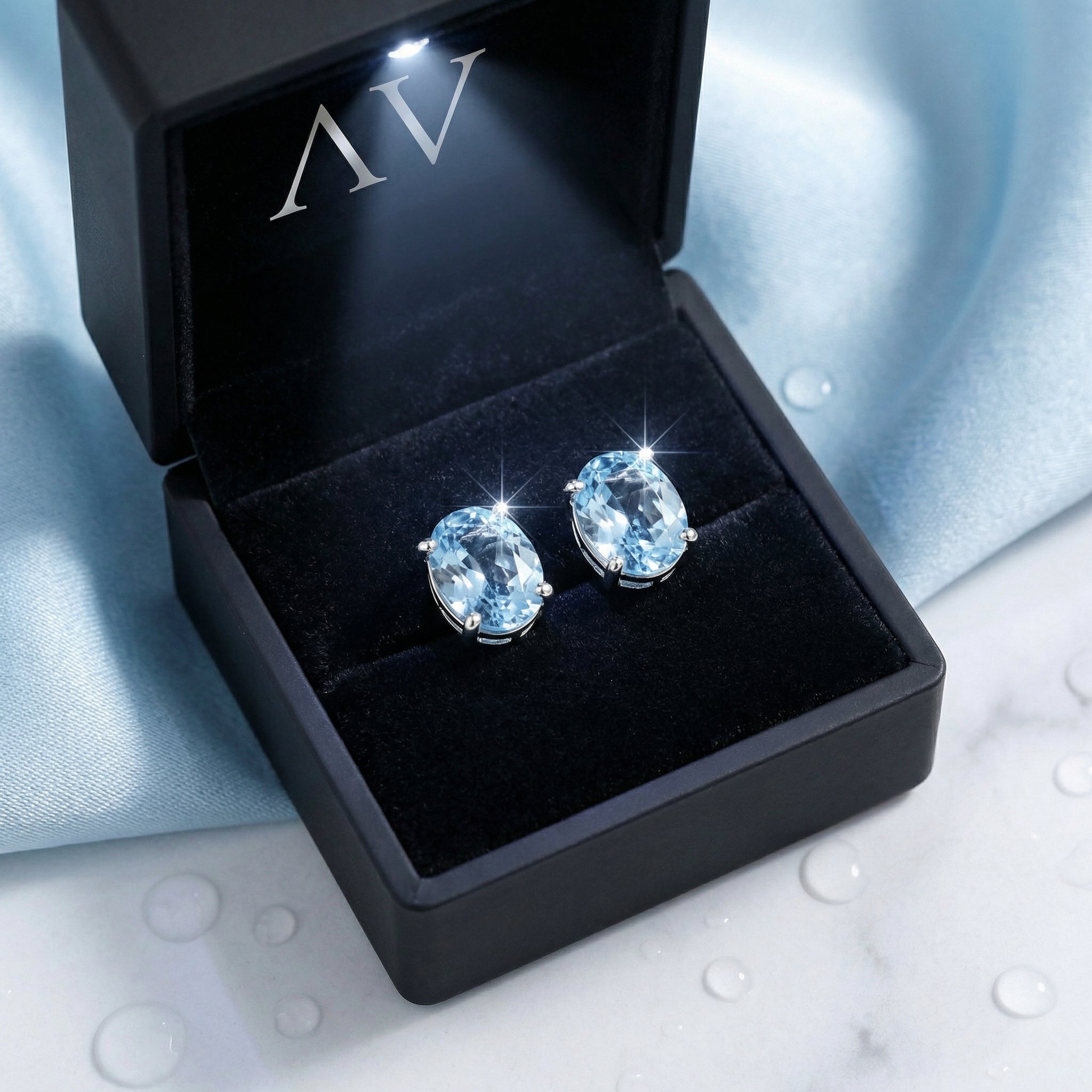 Oval simulated aquamarine sterling silver stud earrings presented in a black lighted jewelry gift box.