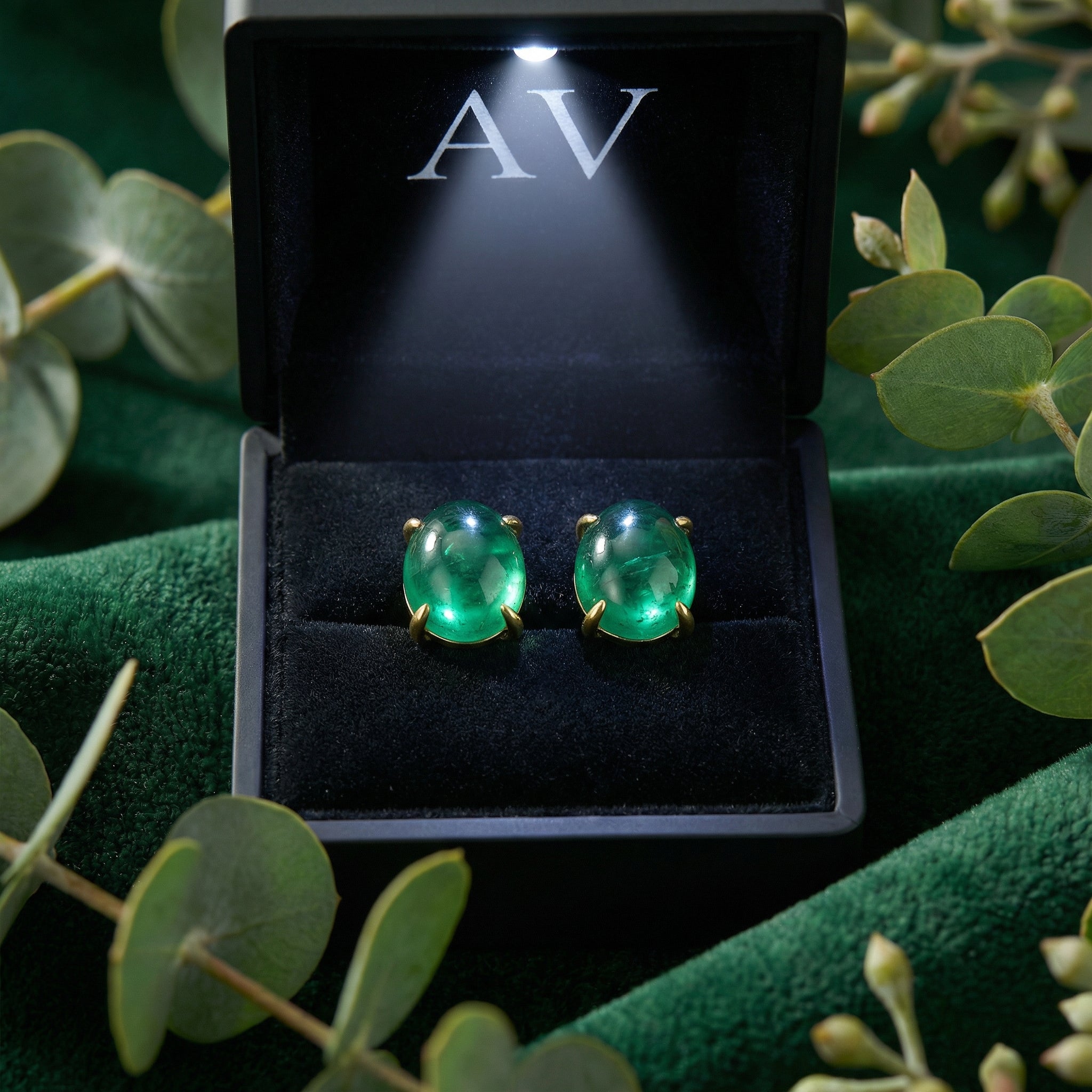 Oval simulated emerald stud earrings in 18K gold vermeil inside a lighted black jewelry box.