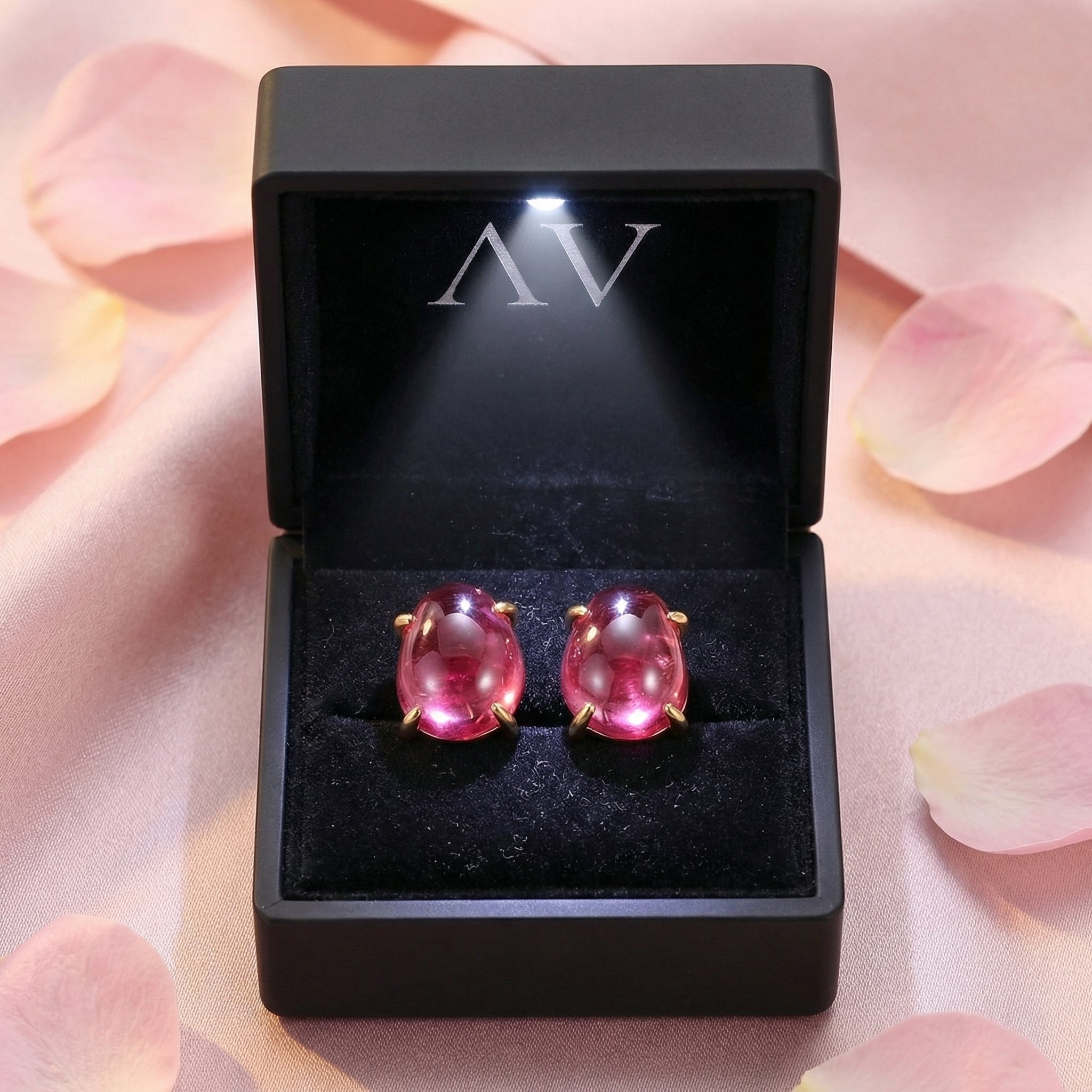 Teardrop simulated pink tourmaline 18K gold vermeil earrings in a lighted black jewelry box with rose petals.