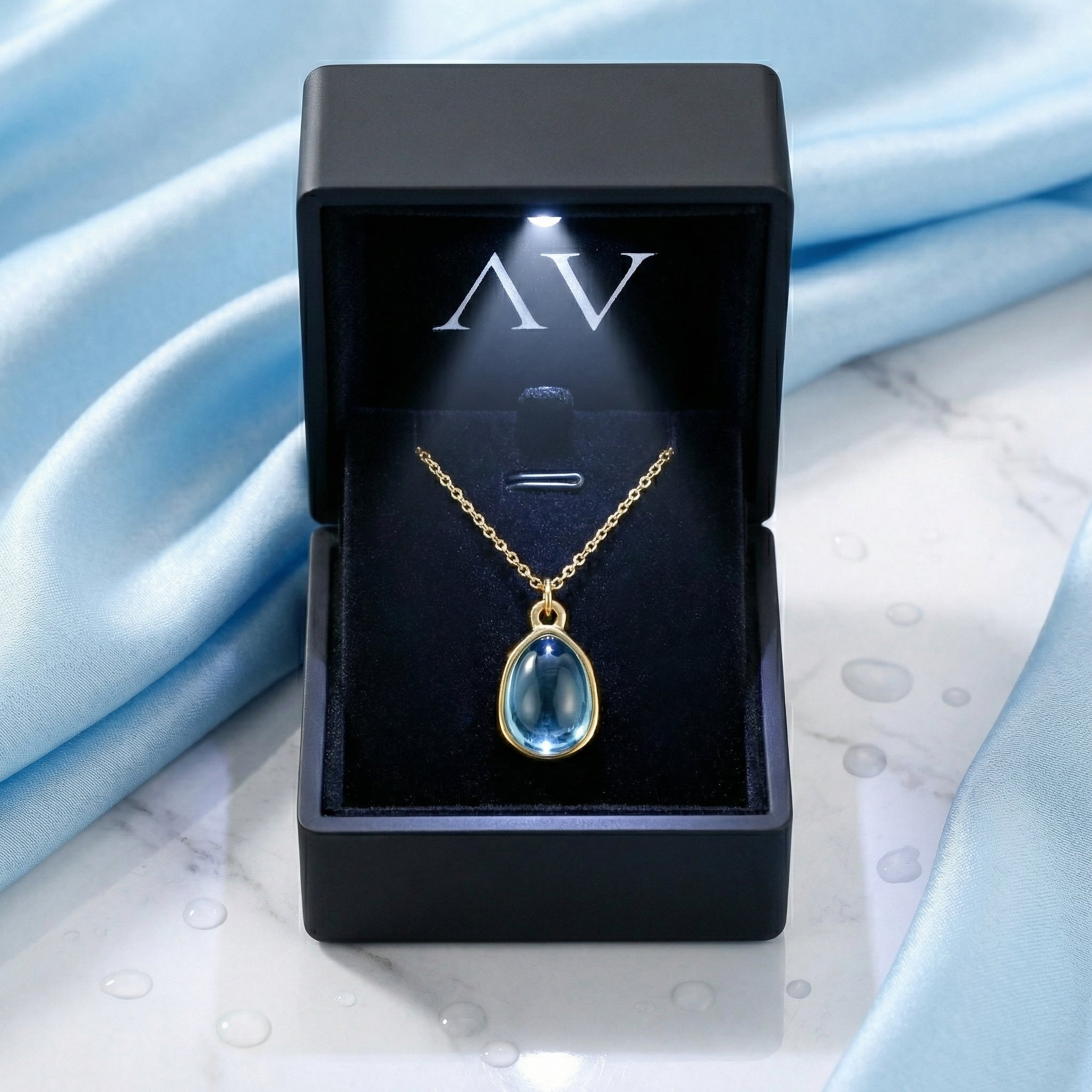 Gold teardrop simulated aquamarine necklace displayed in a black LED-lighted jewelry gift box.