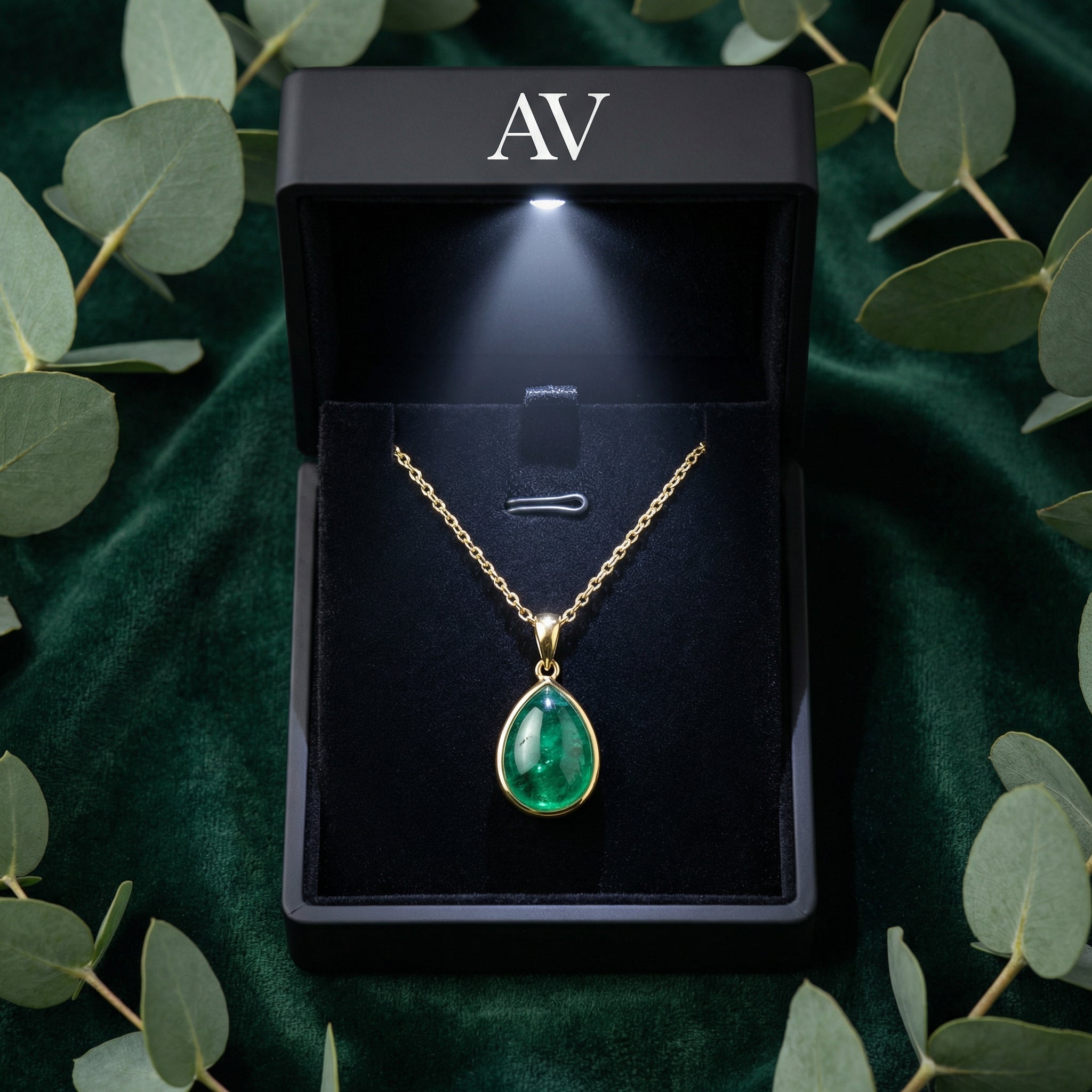 Gold Azurielle teardrop necklace presented in a black LED-lit gift box on green velvet with eucalyptus leaves.
