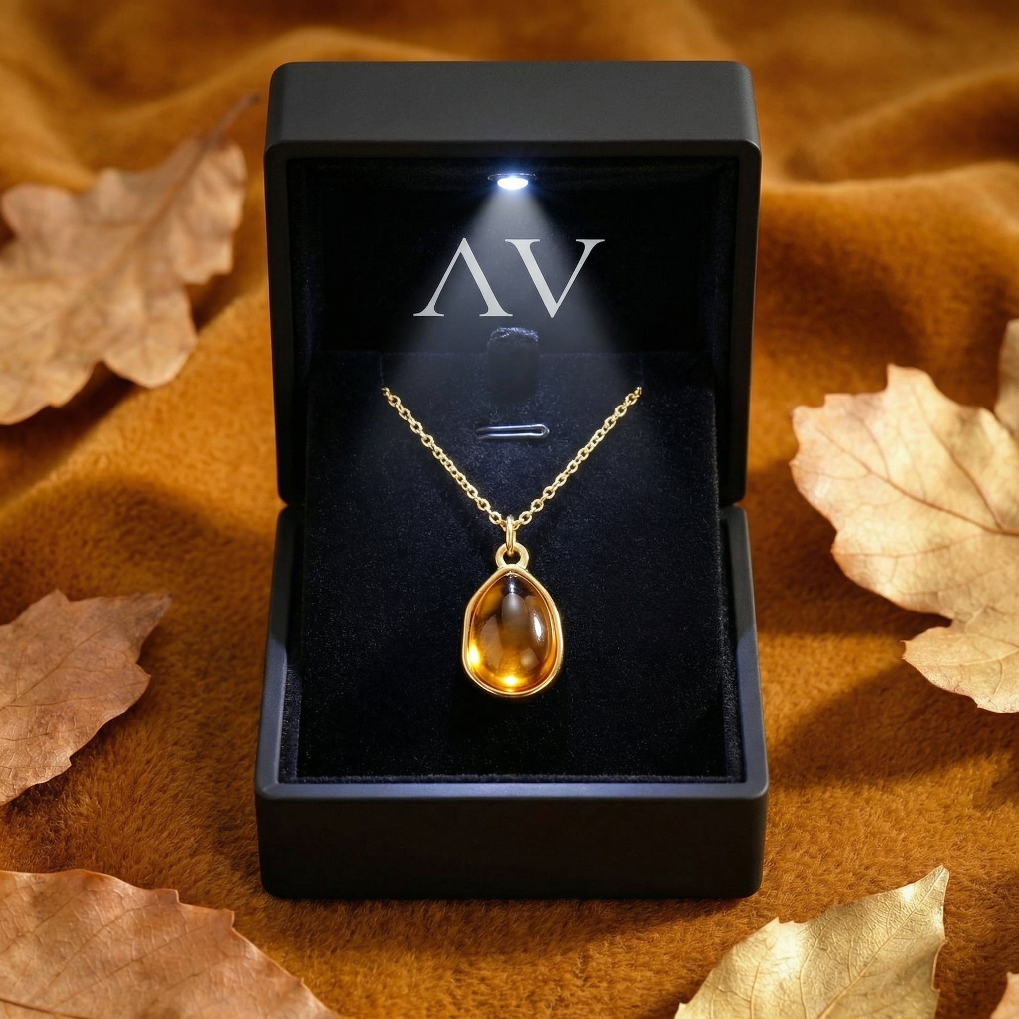Gold finish teardrop simulated topaz necklace in a black LED-lit jewelry gift box with autumn leaves.