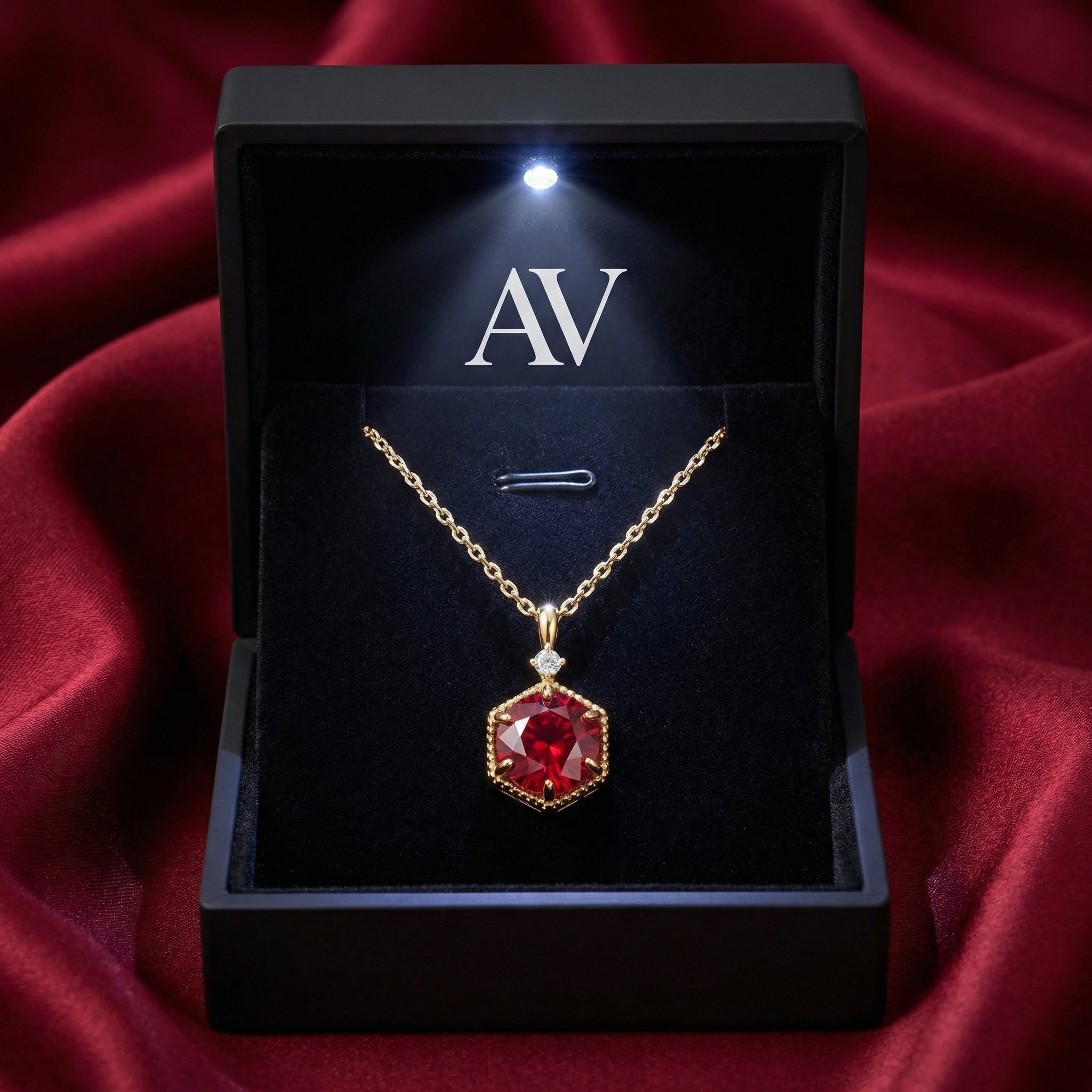 Hexagonal gold vermeil ruby necklace inside a black LED-lighted gift box on red silk.
