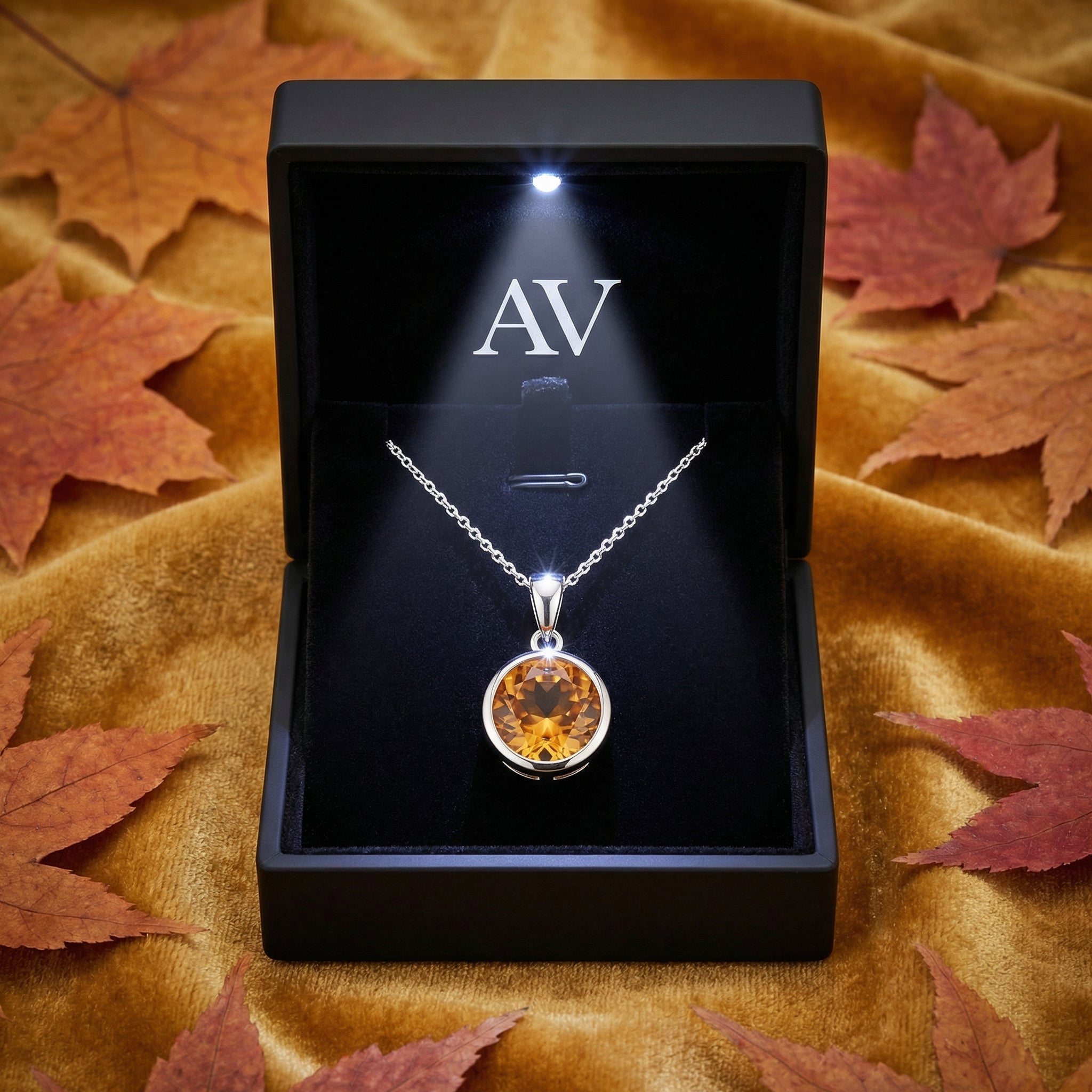 Simulated topaz solitaire necklace in a lighted black gift box surrounded by autumn leaves on velvet.