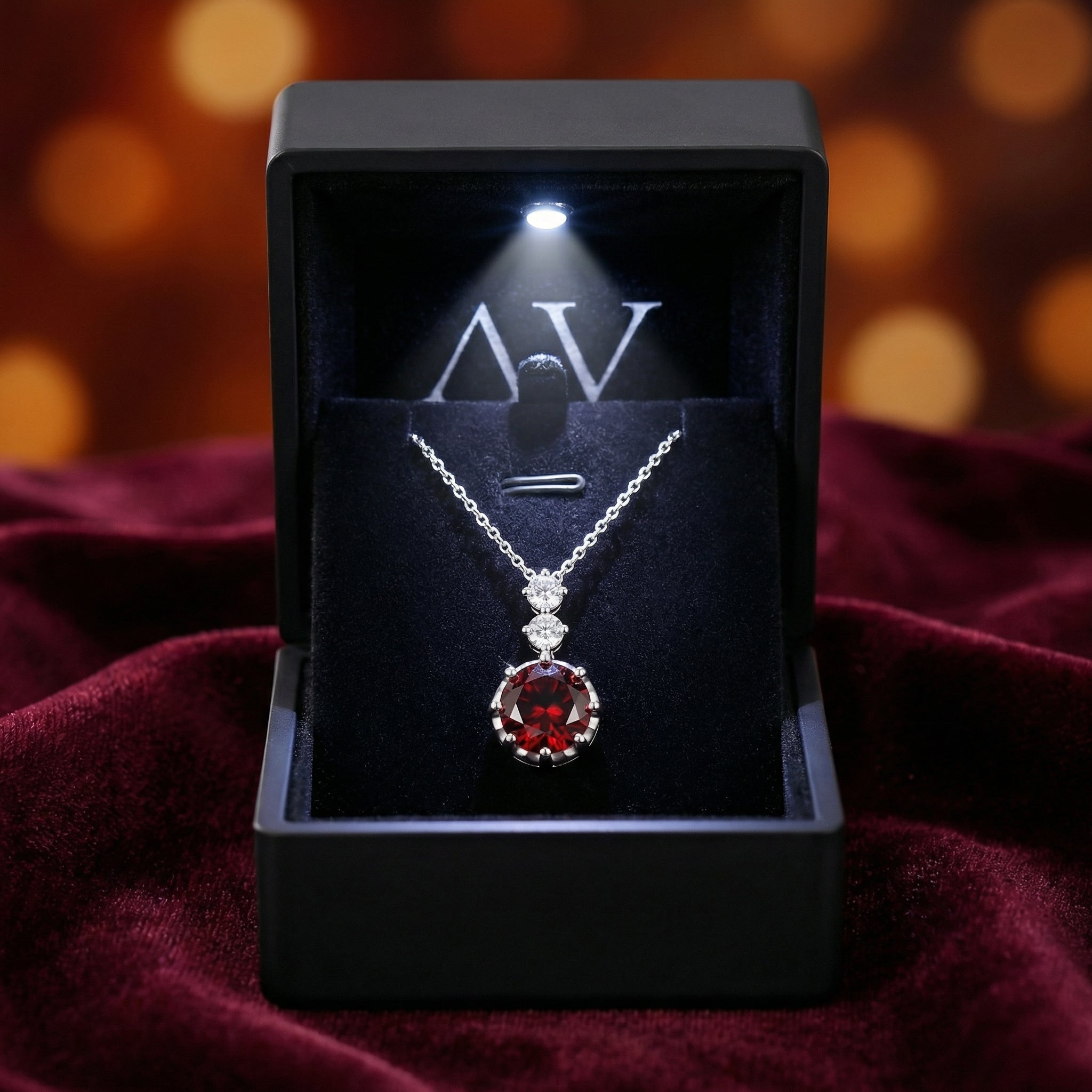 Silver red garnet necklace displayed in a black LED-lit jewelry gift box on a red velvet background.