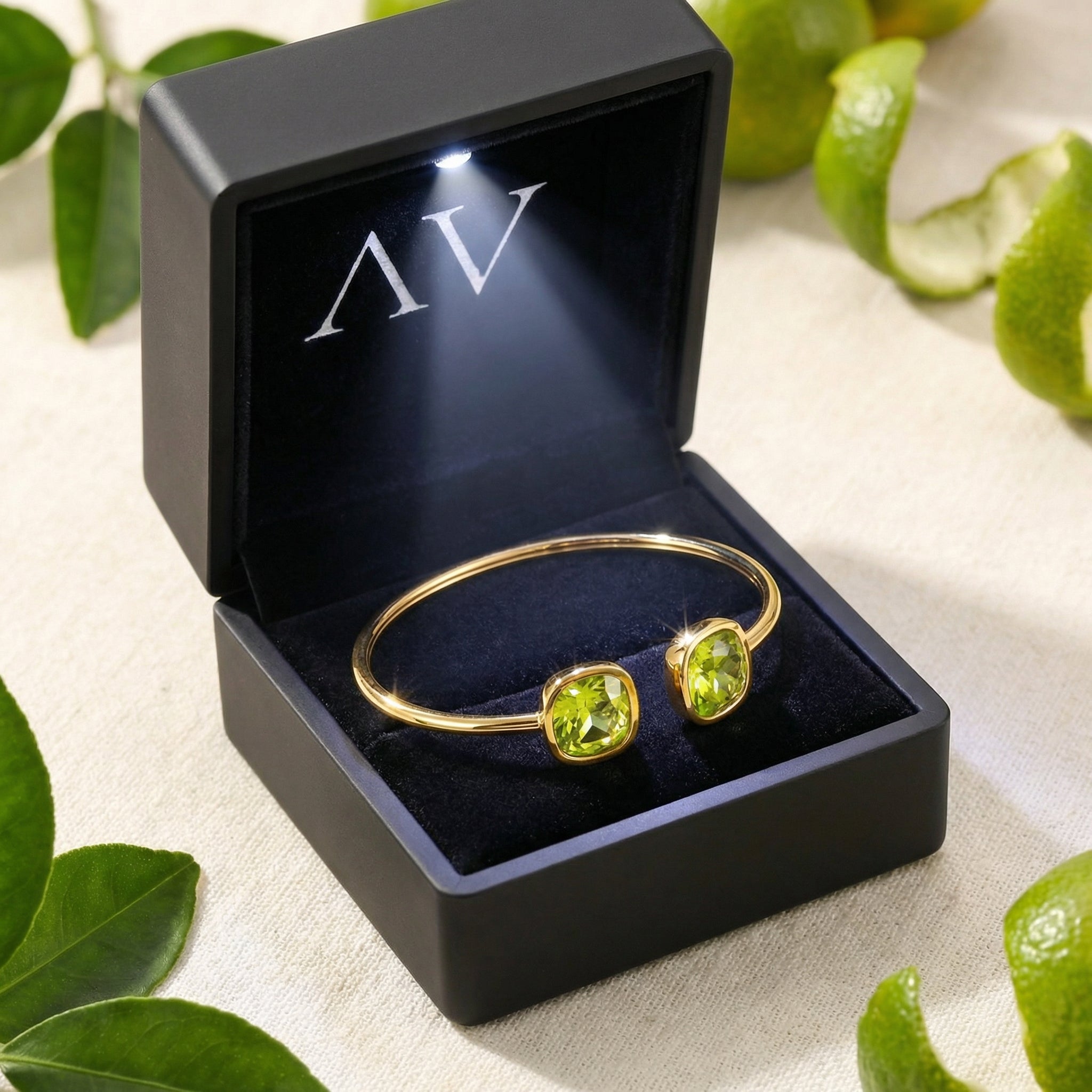 Gold Zelina bangle with simulated peridots inside a black lighted jewelry box with citrus fruit accents.