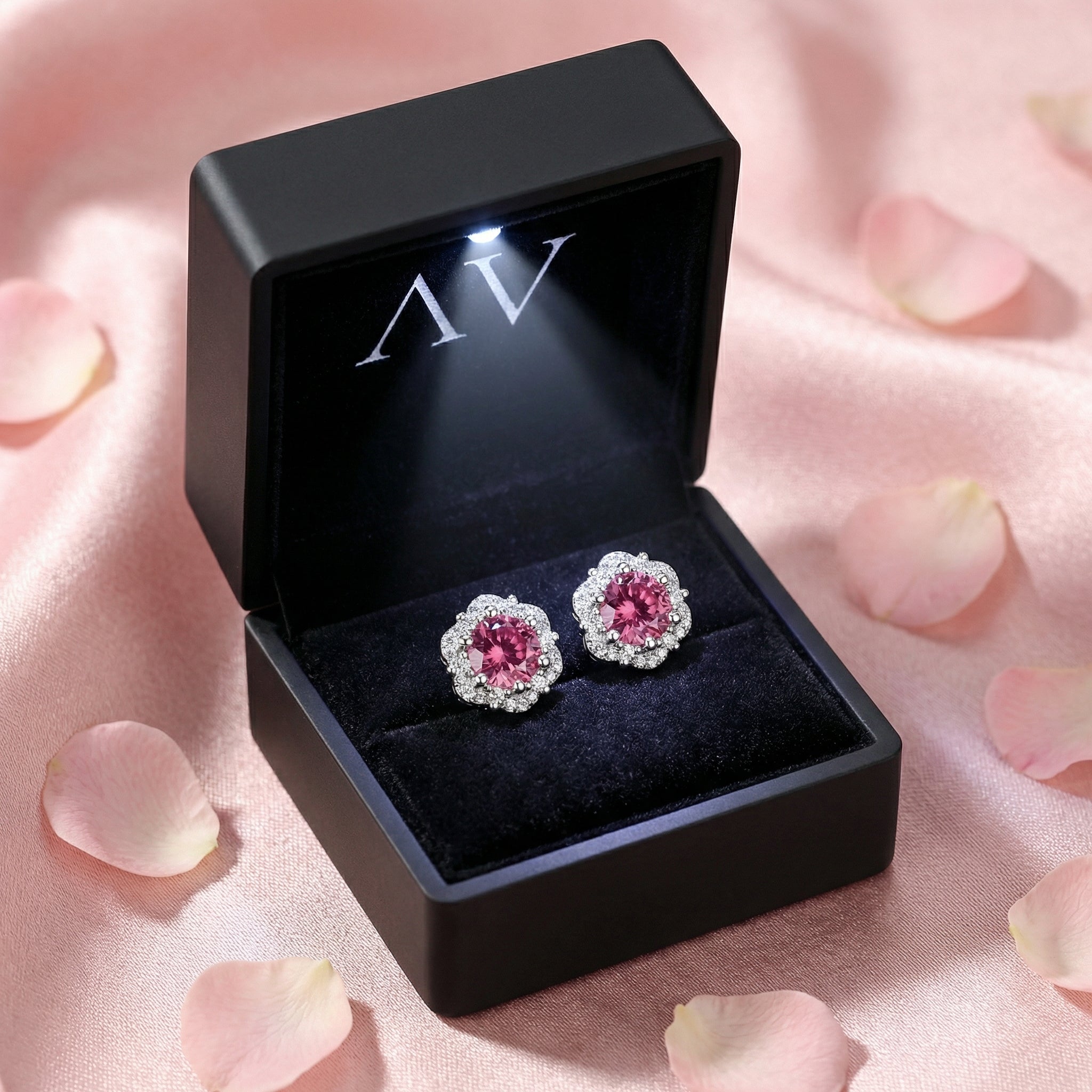 Pair of pink tourmaline halo earrings in a black LED-lit presentation box surrounded by rose petals.