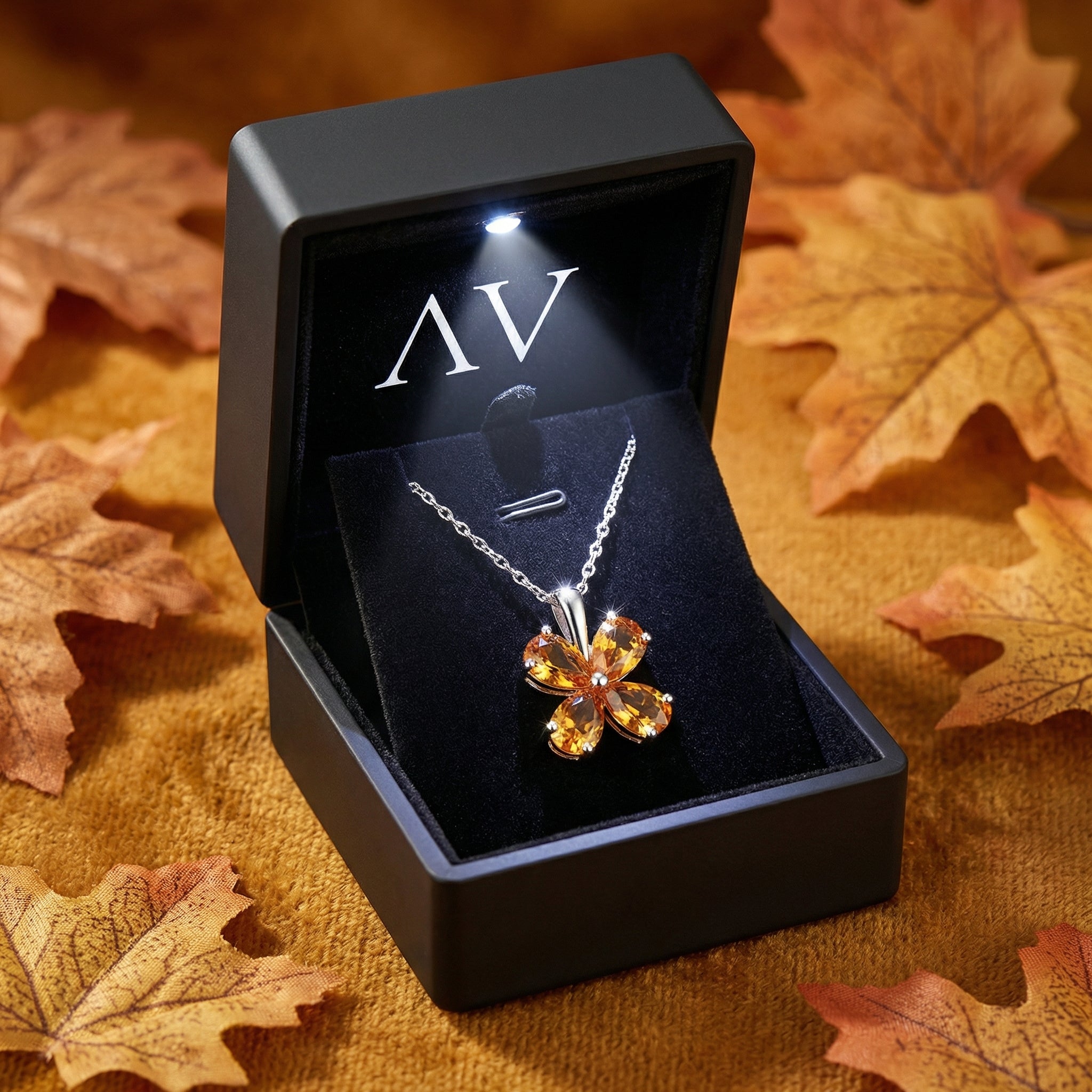 Silver floral necklace with pear-cut orange simulated topaz stones in a lighted black gift box with autumn leaves.