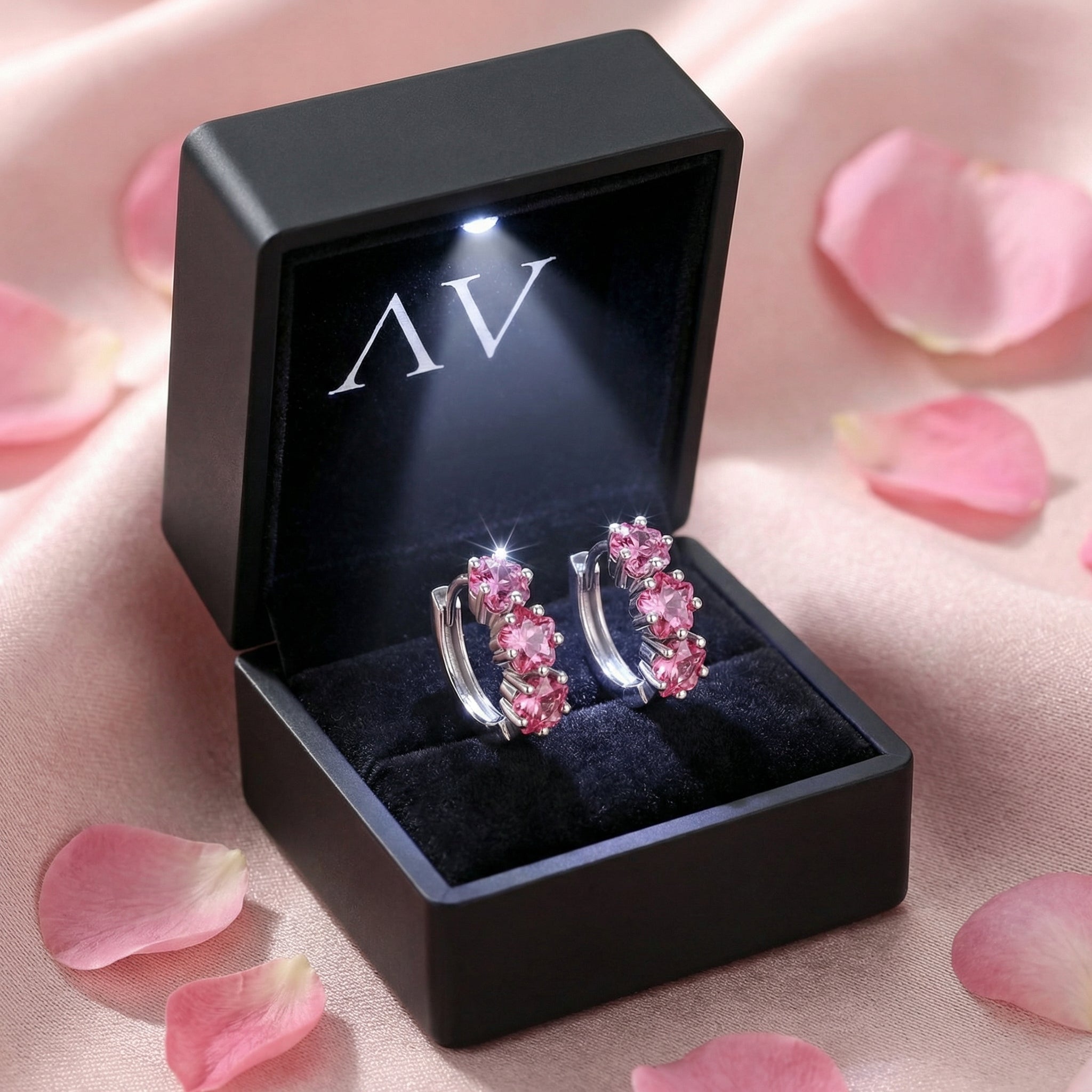Sterling silver pink tourmaline star huggie earrings in a black LED-lighted jewelry box with rose petals.