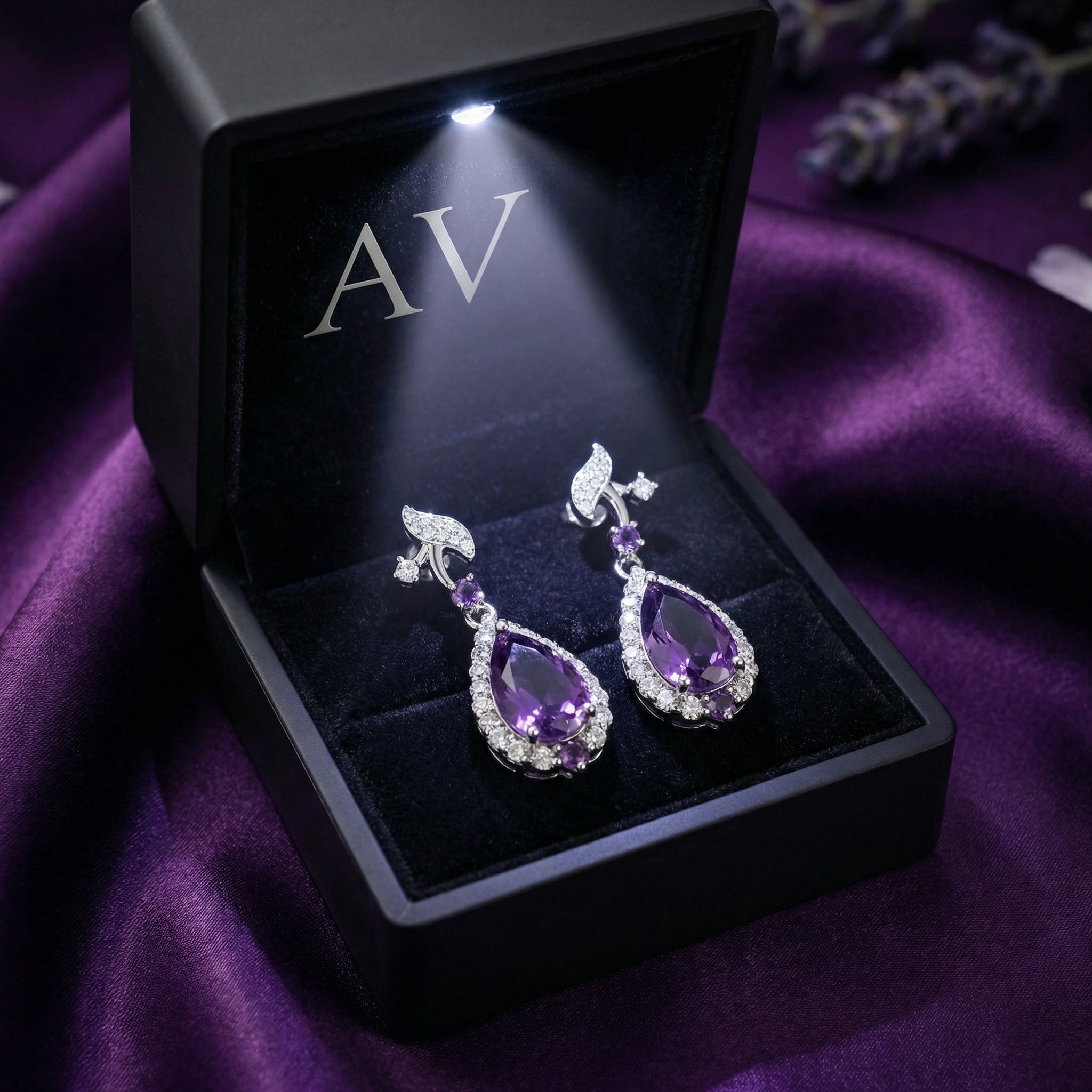 Pair of amethyst drop earrings presented in a black LED-lit gift box on purple silk.
