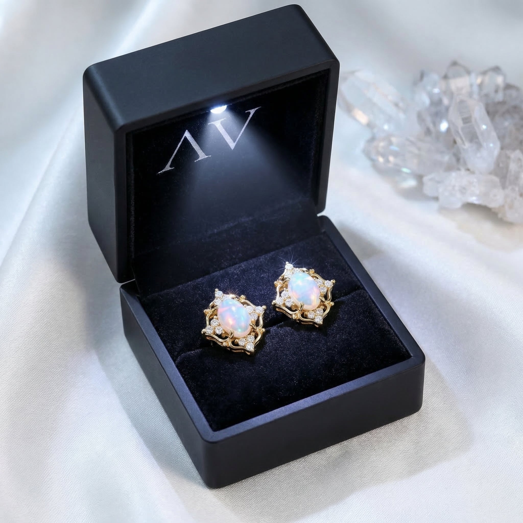 Gold-tone white opal earrings presented in a black LED-lit jewelry gift box on a white silk background.