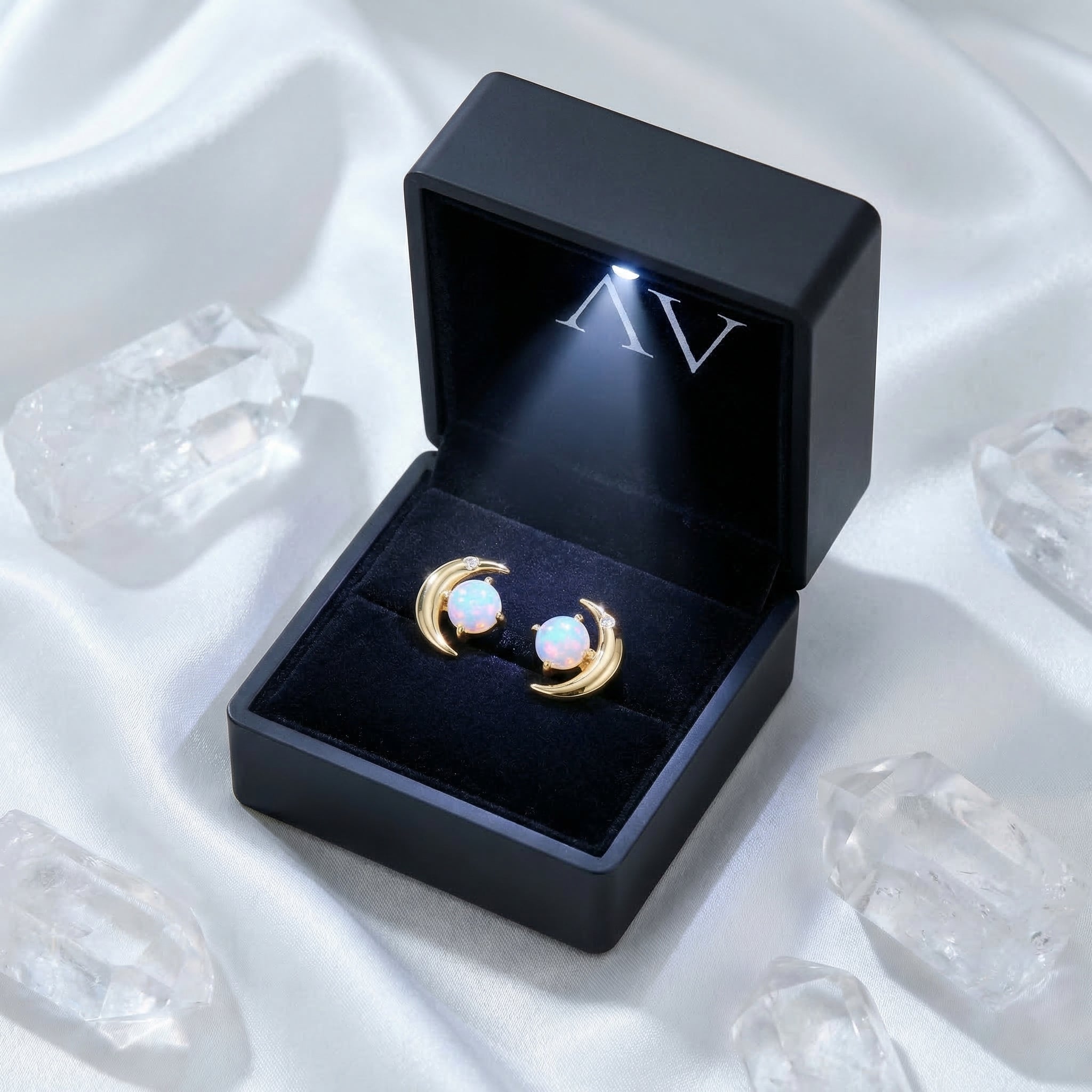 Gold-tone opal crescent moon stud earrings presented in a black LED-lighted jewelry box on white satin.