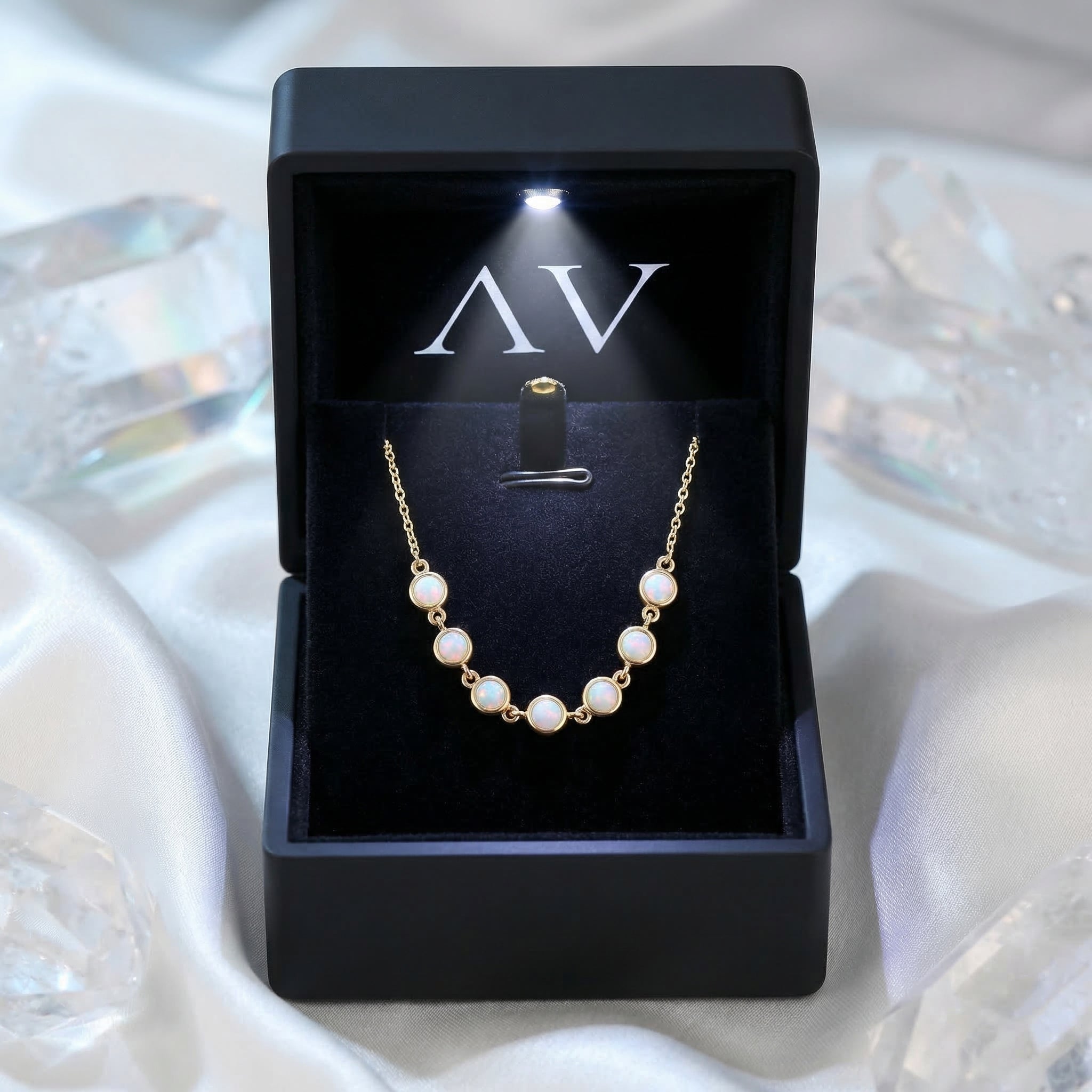 Gold-tone Lumina white opal necklace displayed in a premium black LED-lit jewelry box on white silk.