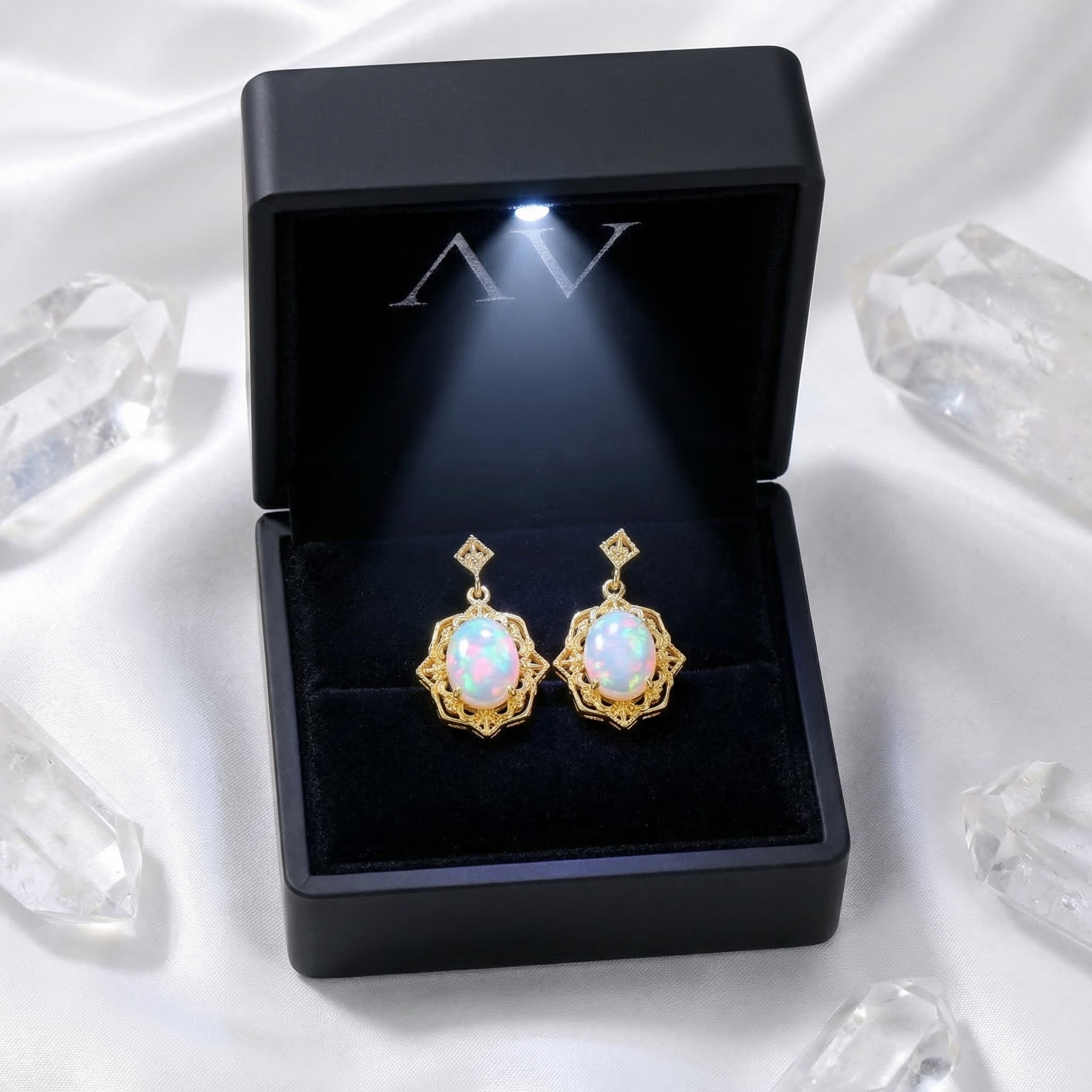 Gold-tone oval white opal drop earrings displayed in a black LED-lighted jewelry gift box.