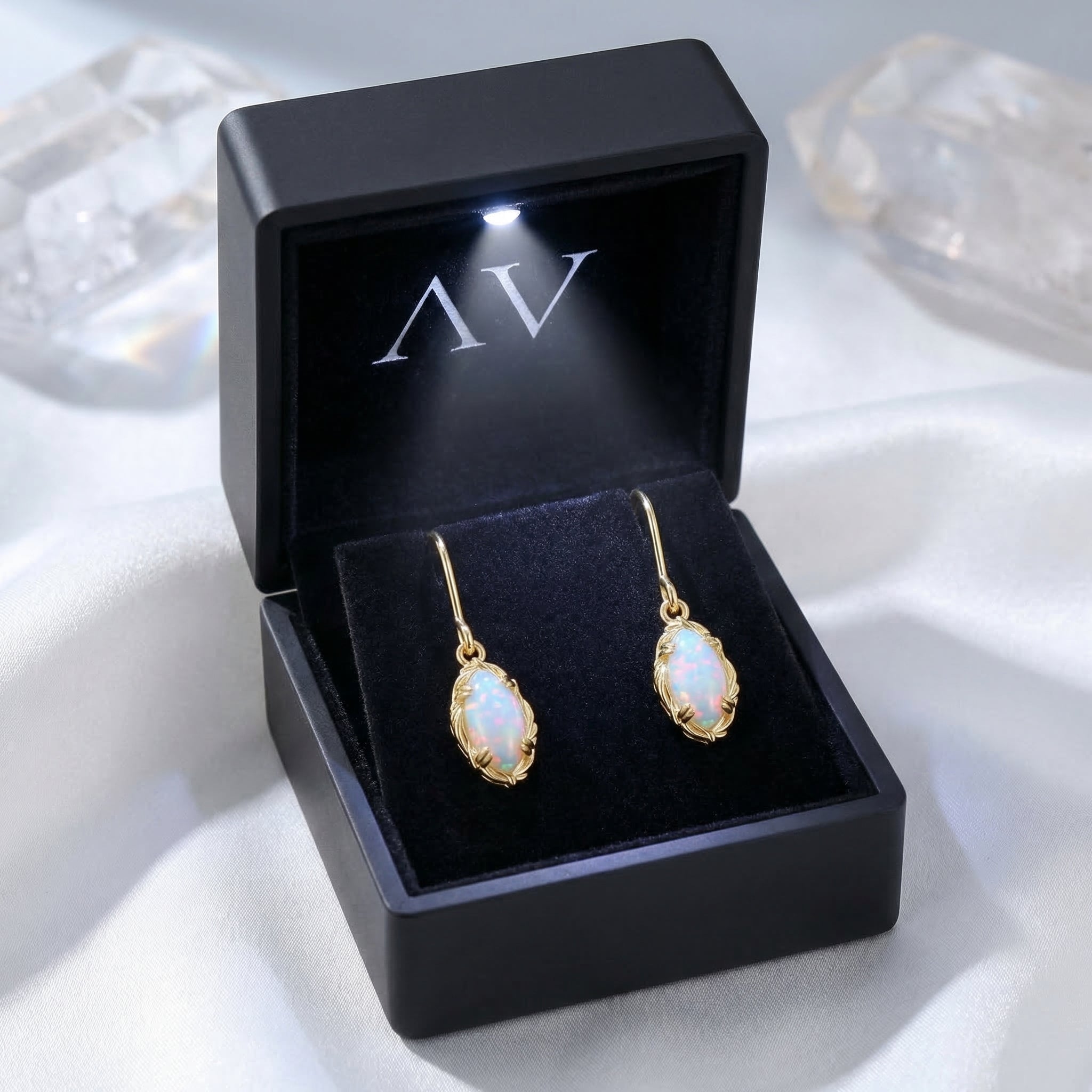 Pair of yellow gold white opal drop earrings inside a black LED-lighted presentation jewelry box.