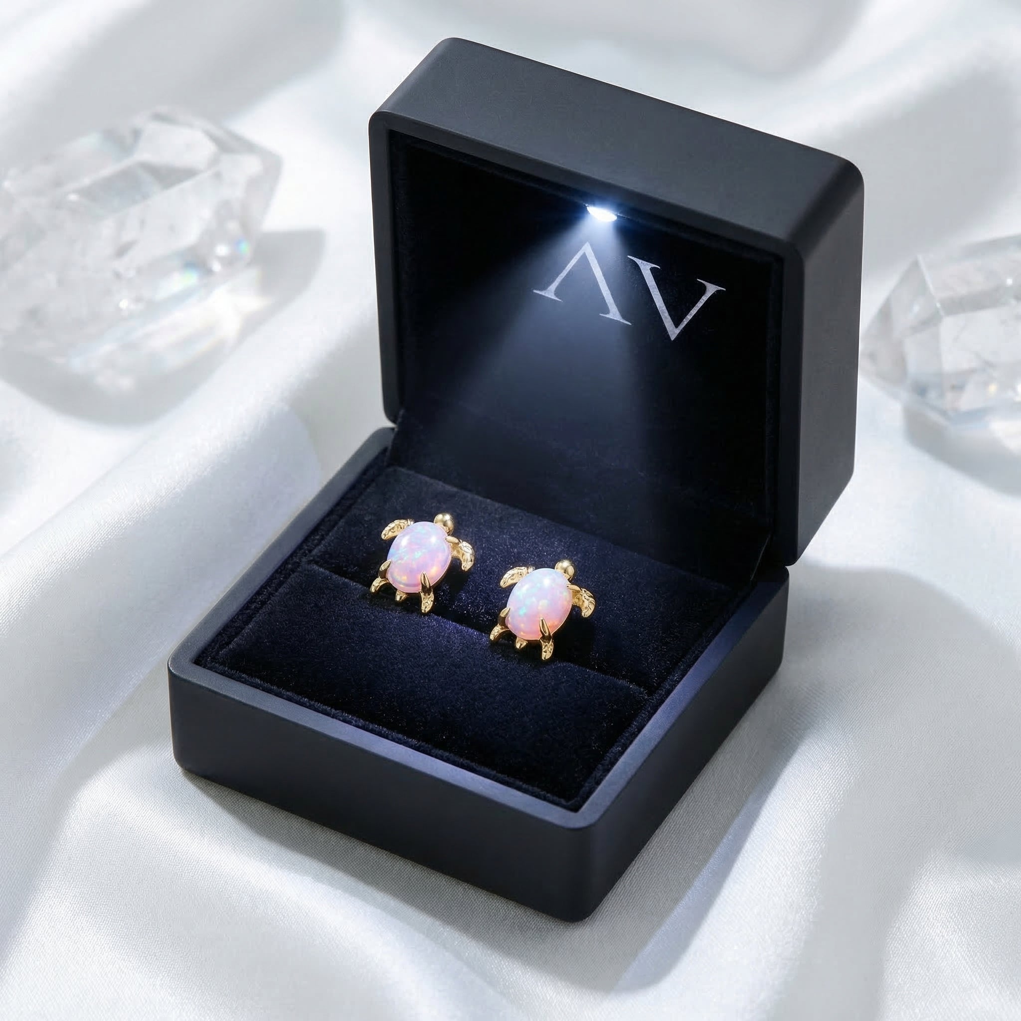 Gold-tone white opal turtle earrings presented in a black LED-lit jewelry gift box on white silk.