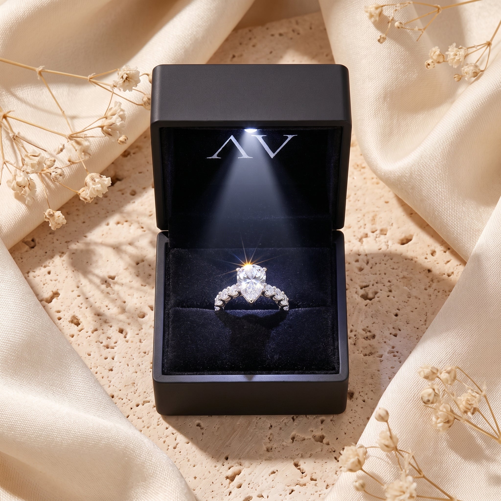 Silver pear-cut solitaire ring inside a lighted black gift box.