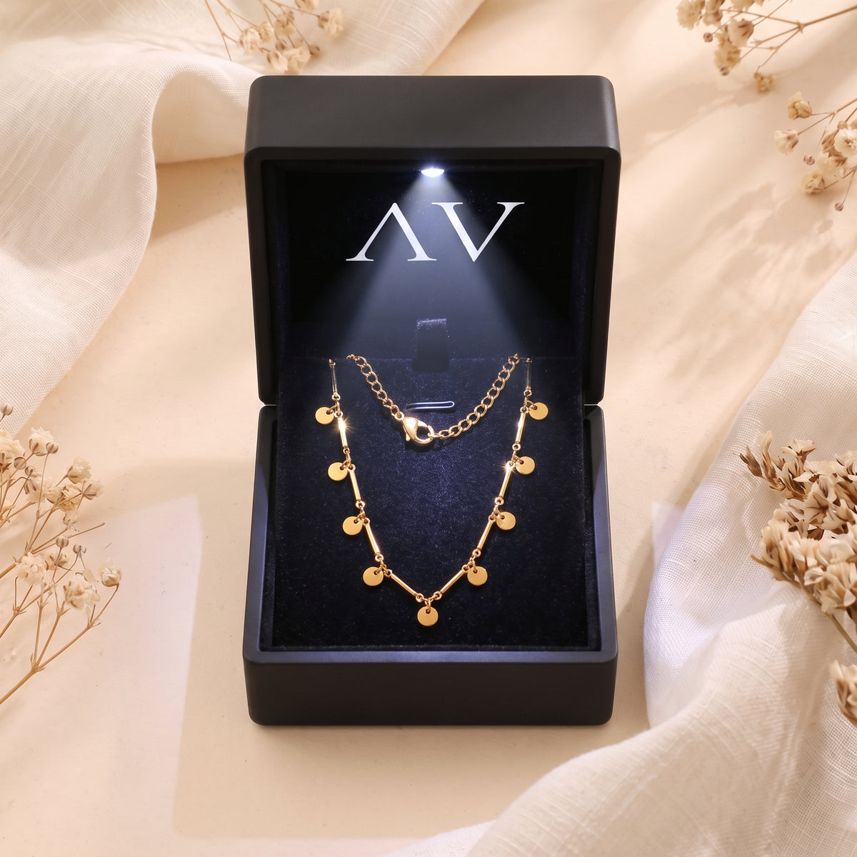 Gold disc necklace in a black LED-lit jewelry box.