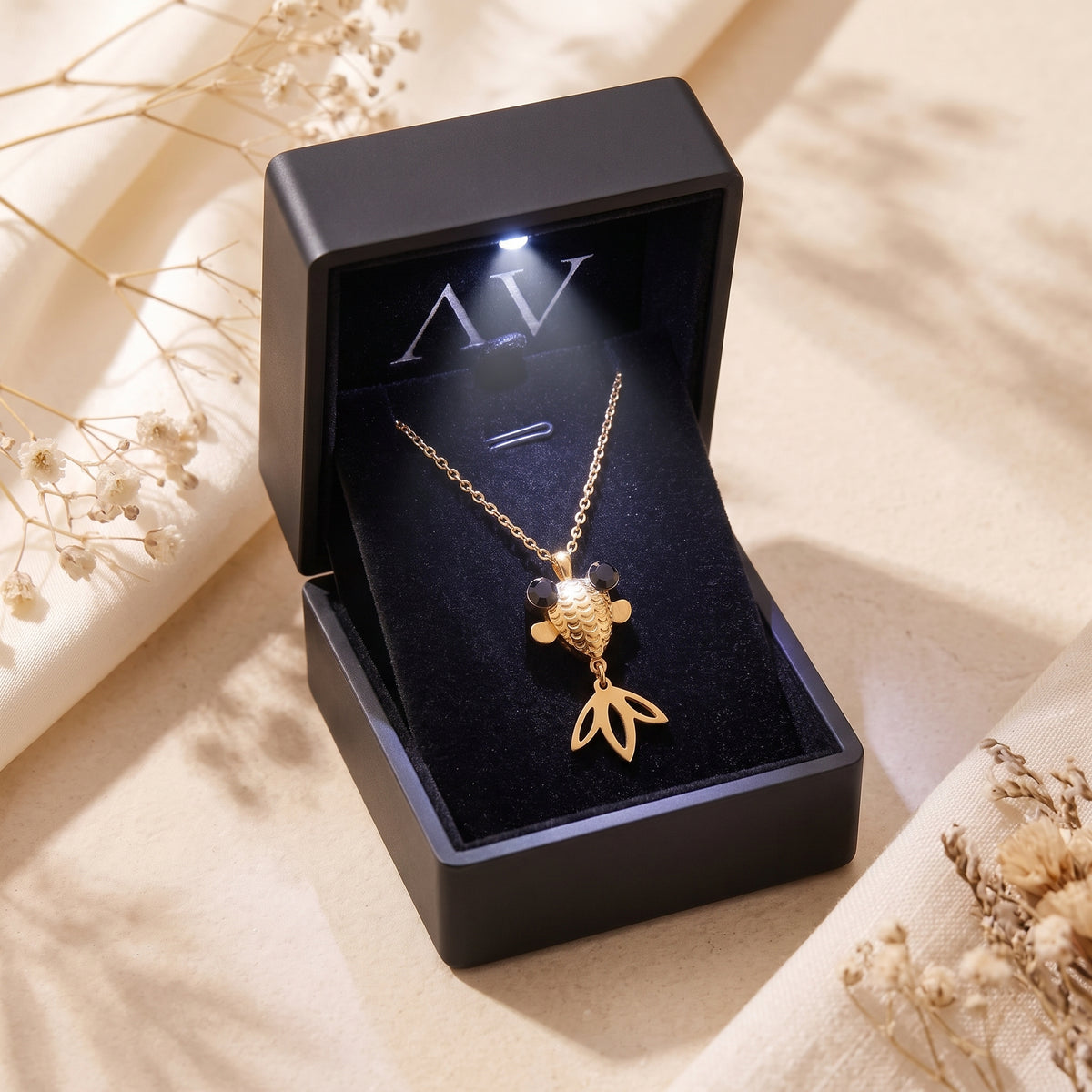 Gold finish goldfish necklace presented in a black lighted jewelry box on a neutral background.