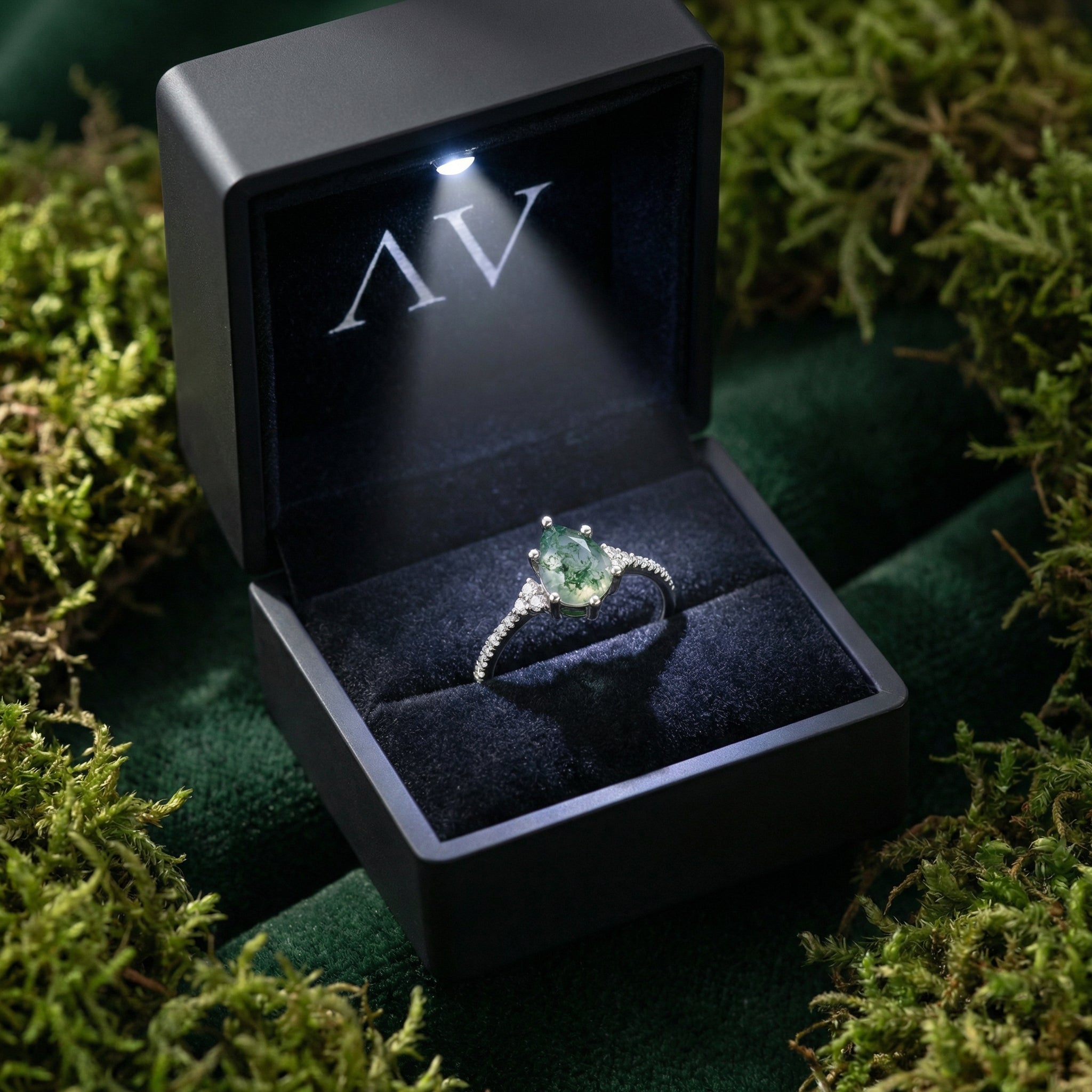 Pear cut moss agate ring presented in a black lighted gift box on a bed of green moss.