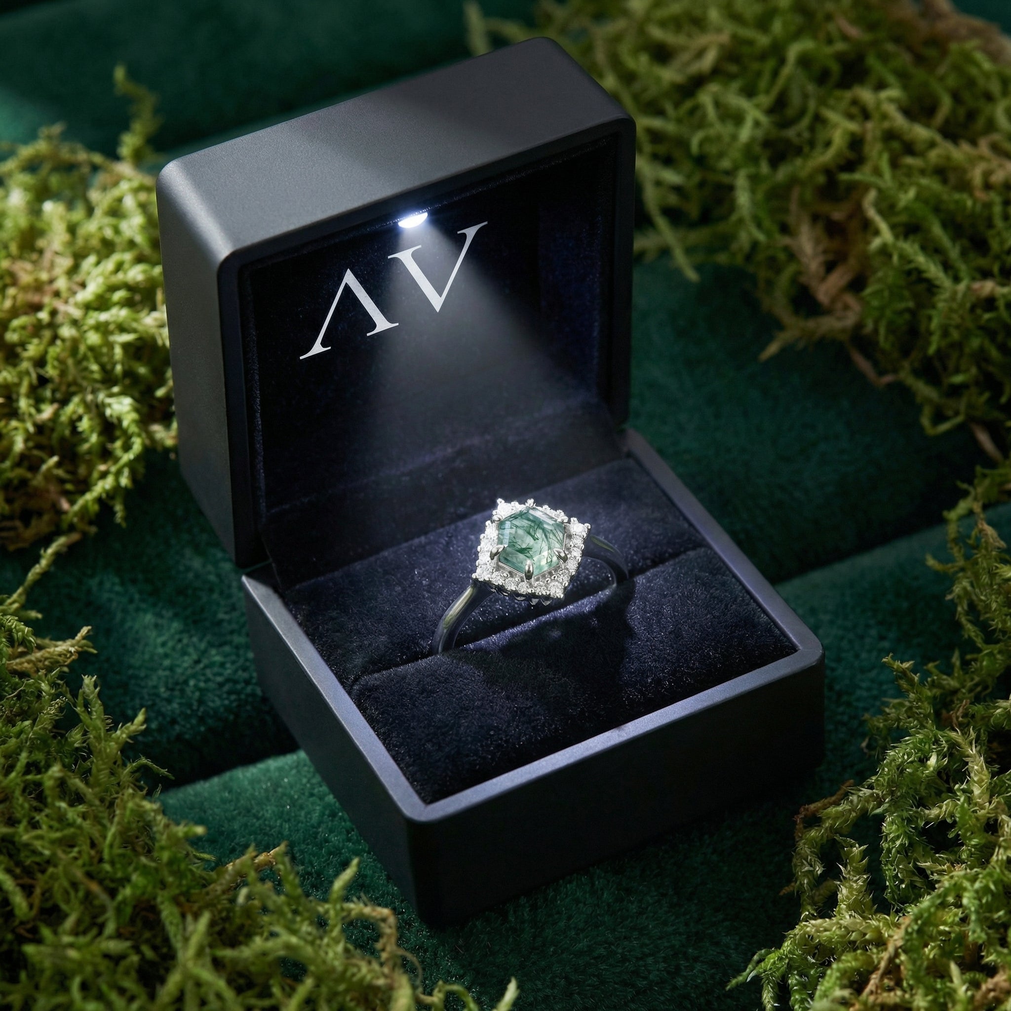 Hexagonal moss agate ring in a lighted black gift box surrounded by natural green moss.