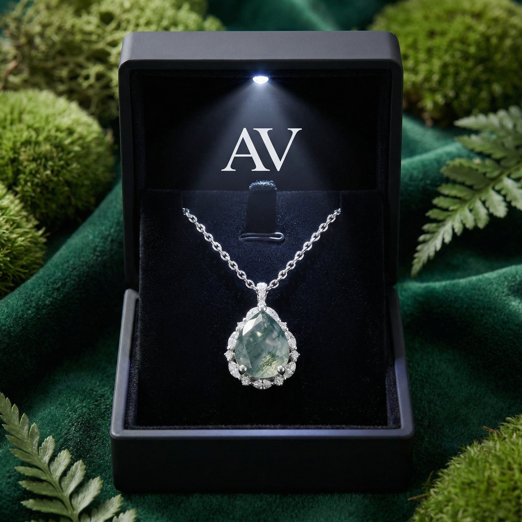 Teardrop moss agate necklace in a lighted black jewelry gift box with AV branding on a mossy background.