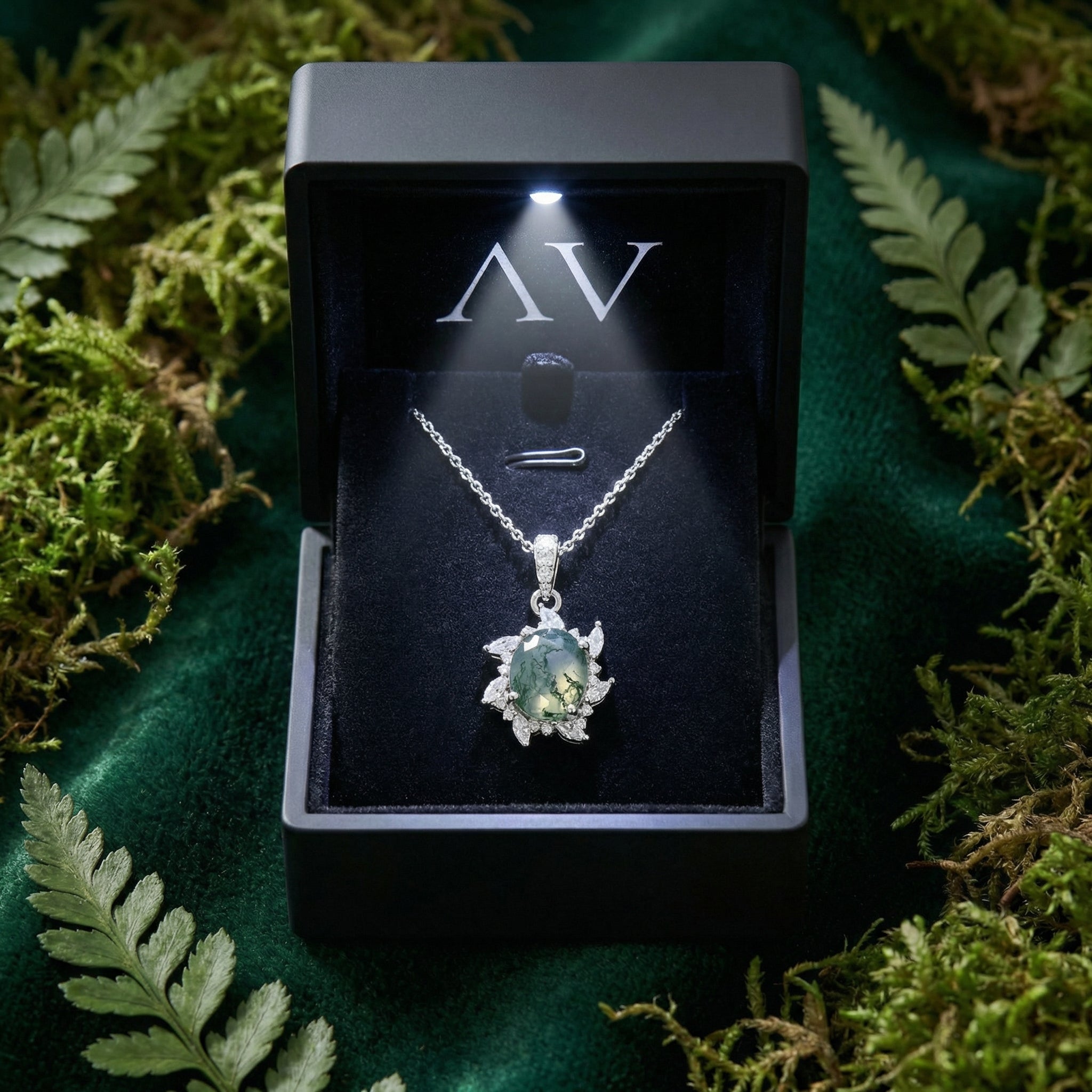 Starburst moss agate necklace displayed in a black LED-lighted gift box on a mossy background.