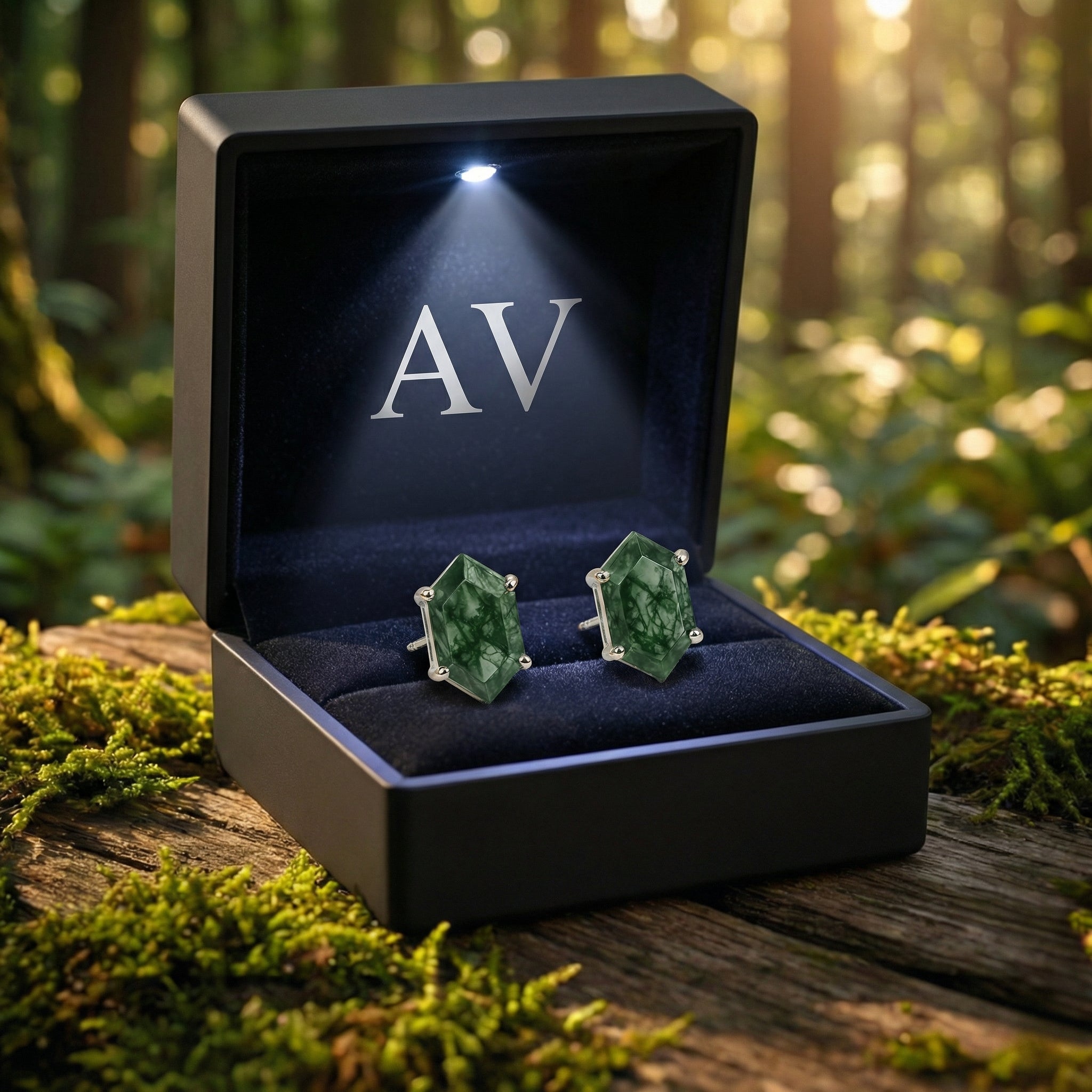 Hexagon moss agate earrings in a black LED-lit gift box with AV logo, placed on a mossy log in the woods.