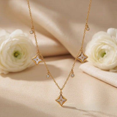 Gold-tone star pendant necklace with clear dangling accents displayed on beige fabric between white flowers