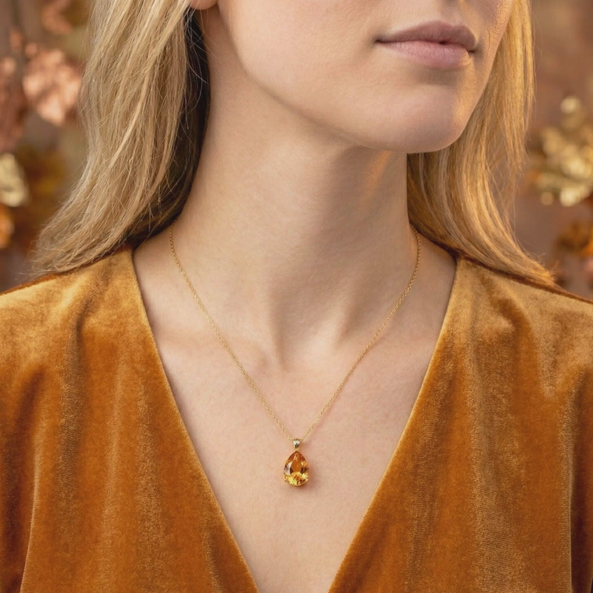 Woman wearing a teardrop simulated topaz pendant necklace with a solid gold chain over a velvet garment.