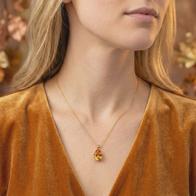 Woman wearing a teardrop simulated topaz pendant necklace with a solid gold chain over a velvet garment.