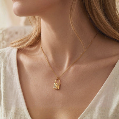 Gold-toned padlock pendant necklace with crescent moon and star details, shown worn on a person's neck.