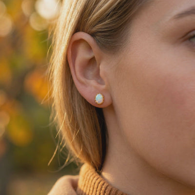 Side-profile close-up of an oval white opal stud earring in a solid gold setting worn on an earlobe.
