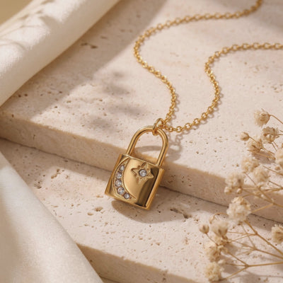 Gold-toned padlock pendant necklace with stone-set crescent moon and star, displayed on a textured stone surface.