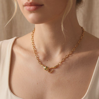 Yellow gold-tone link necklace with a green-eyed snake clasp worn around a model’s neck over a cream top.