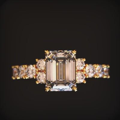 A solid gold ring with an emerald-cut center stone and round accent gems on a dark surface.