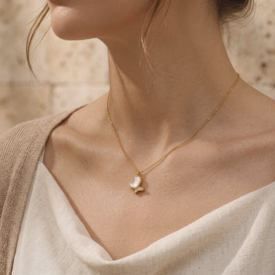 Model wearing a gold-tone necklace with a mother-of-pearl butterfly pendant and clear accent stones.