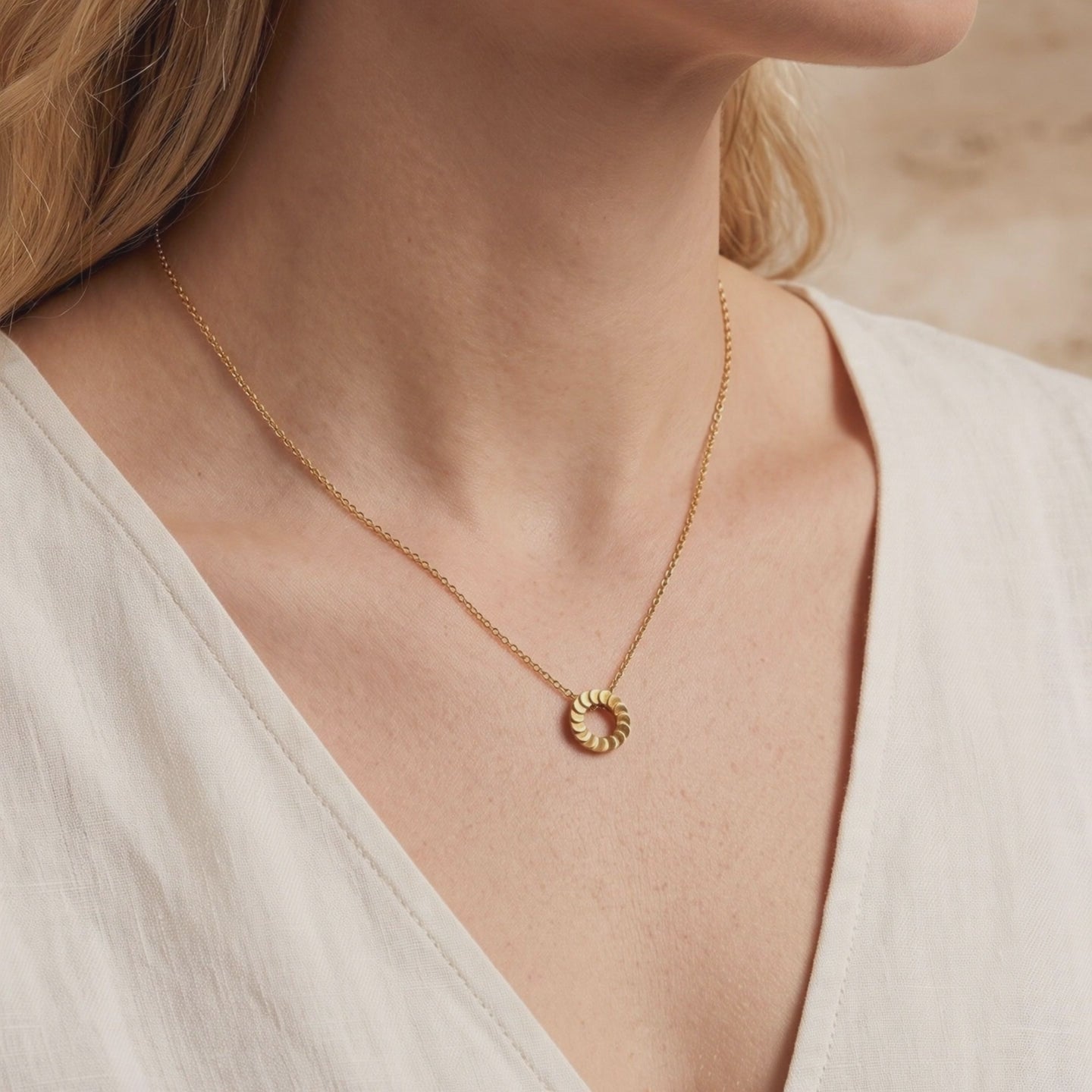 Gold-tone circular pendant necklace with overlapping disks, worn on a woman's neckline over a white V-neck top.