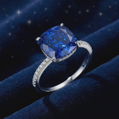 Close-up of a cushion-cut blue simulated sapphire ring with a micro-pavé solid white gold band.