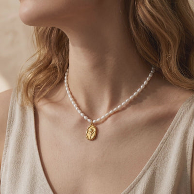 Model wearing a pearl necklace with a gold-toned oval pendant featuring a rose motif.