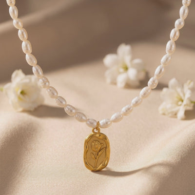 Pearl necklace arranged on soft fabric with a gold-toned rose pendant and white flowers nearby.