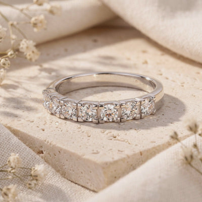 Evadienne silver eternity ring with round clear stones on a textured beige stone slab with small white flowers